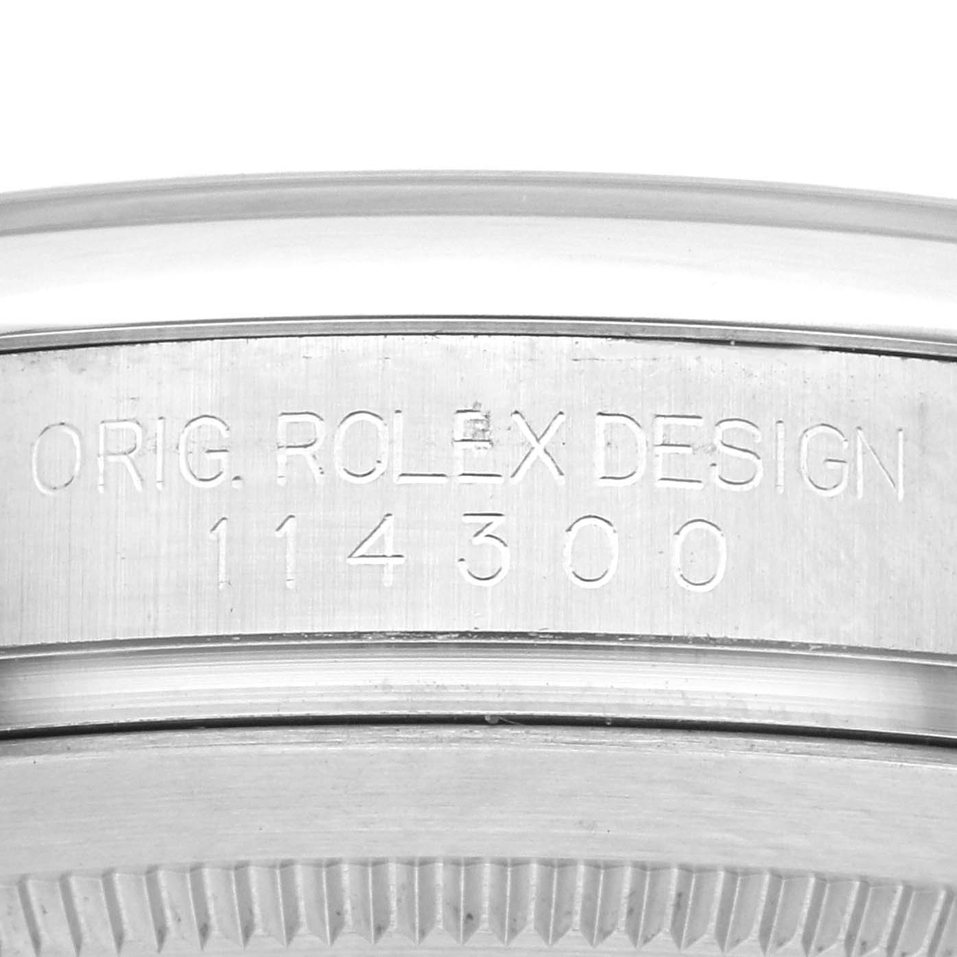 The image shows a close-up of the side of a Rolex Oyster Perpetual 114300 Men's Stainless Steel Blue Dial 114300 Men's Stainless Steel Blue Dial watch, highlighting the model number and engraving.