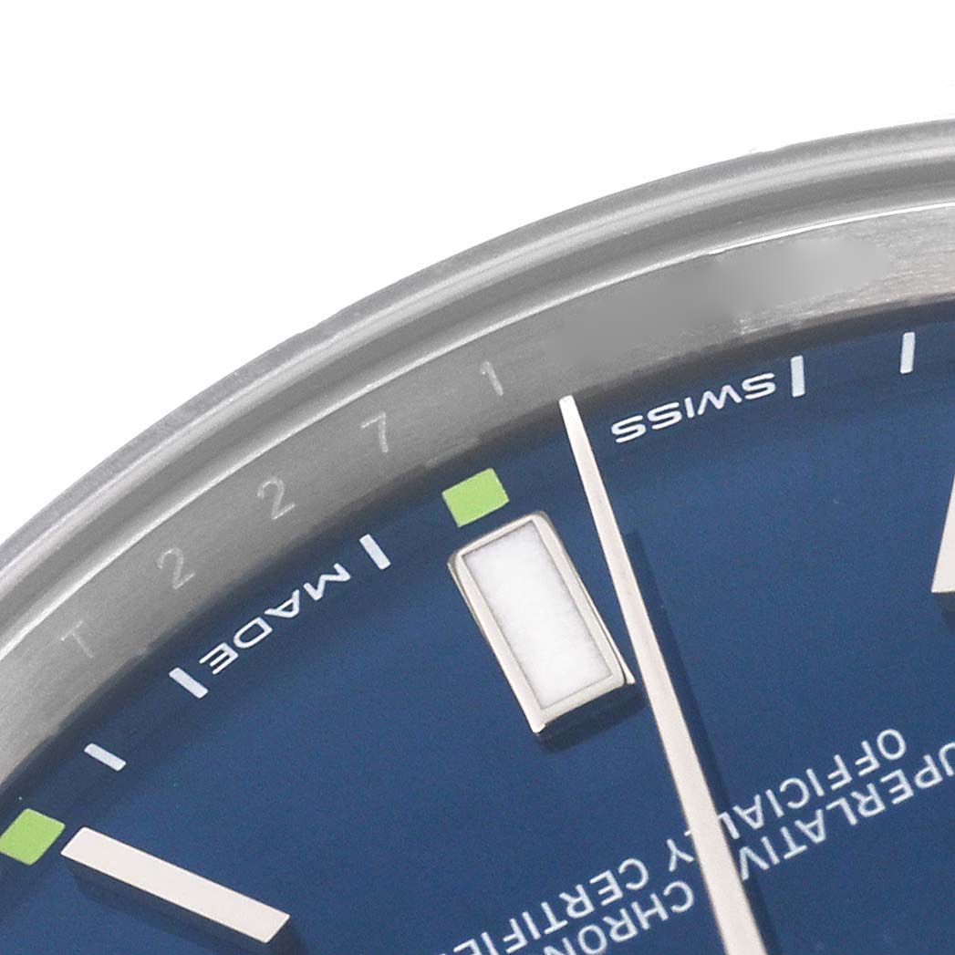 The image shows a close-up of the Rolex Oyster Perpetual 114300 Men's Stainless Steel Blue Dial 114300 Men's Stainless Steel Blue Dial's blue dial, including part of the bezel, hour markers, and text.