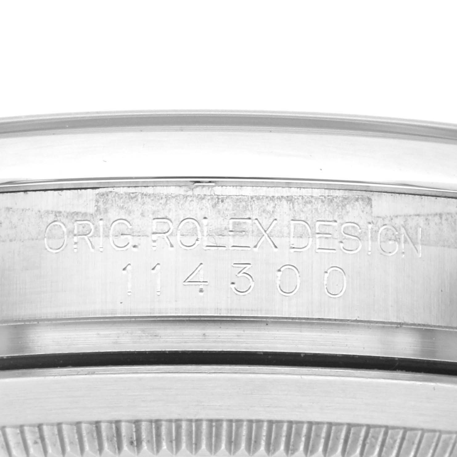 The angle shows a close-up of the side of a Rolex Oyster Perpetual 114300 Men's Stainless Steel Red Dial 114300 Men's Stainless Steel Red Dial, focusing on the model number engraving.