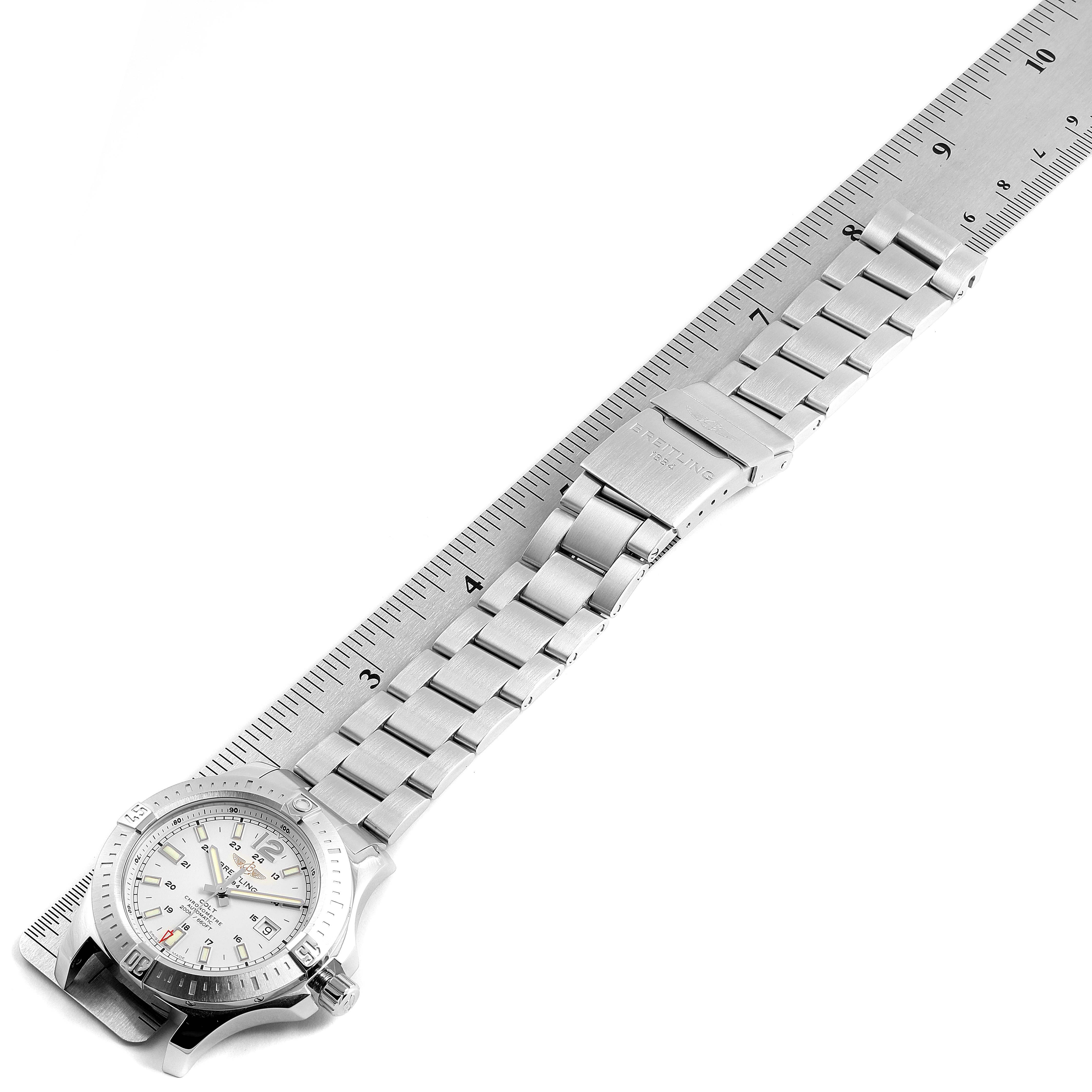 The image shows a top view of a Breitling Colt A17388 Men's Stainless Steel White Dial A17388 Men's Stainless Steel White Dial watch with a metal bracelet laying alongside a ruler.