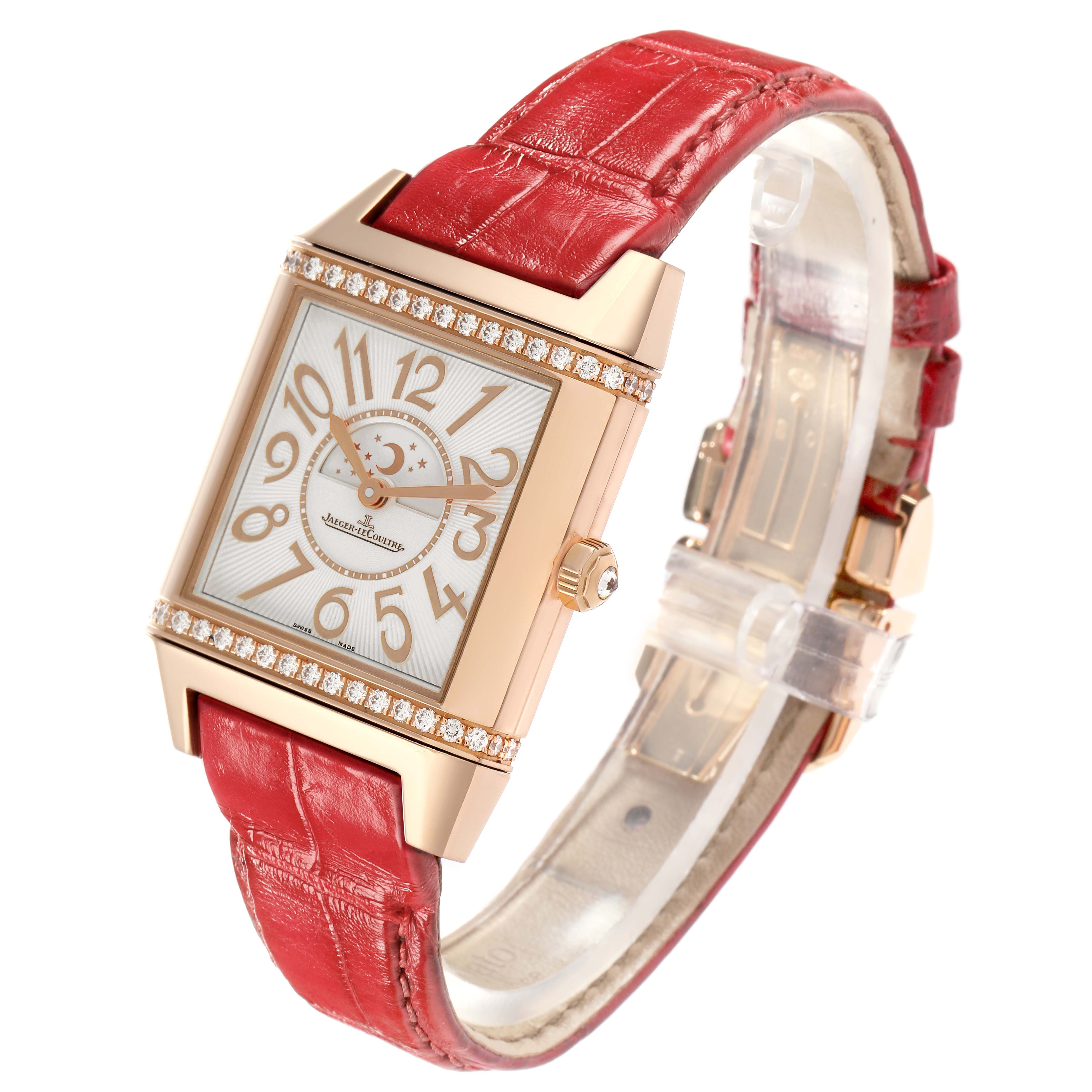 The Jaeger-LeCoultre Reverso watch is shown at an angled view, highlighting its rectangular case, red strap, and diamond accents.