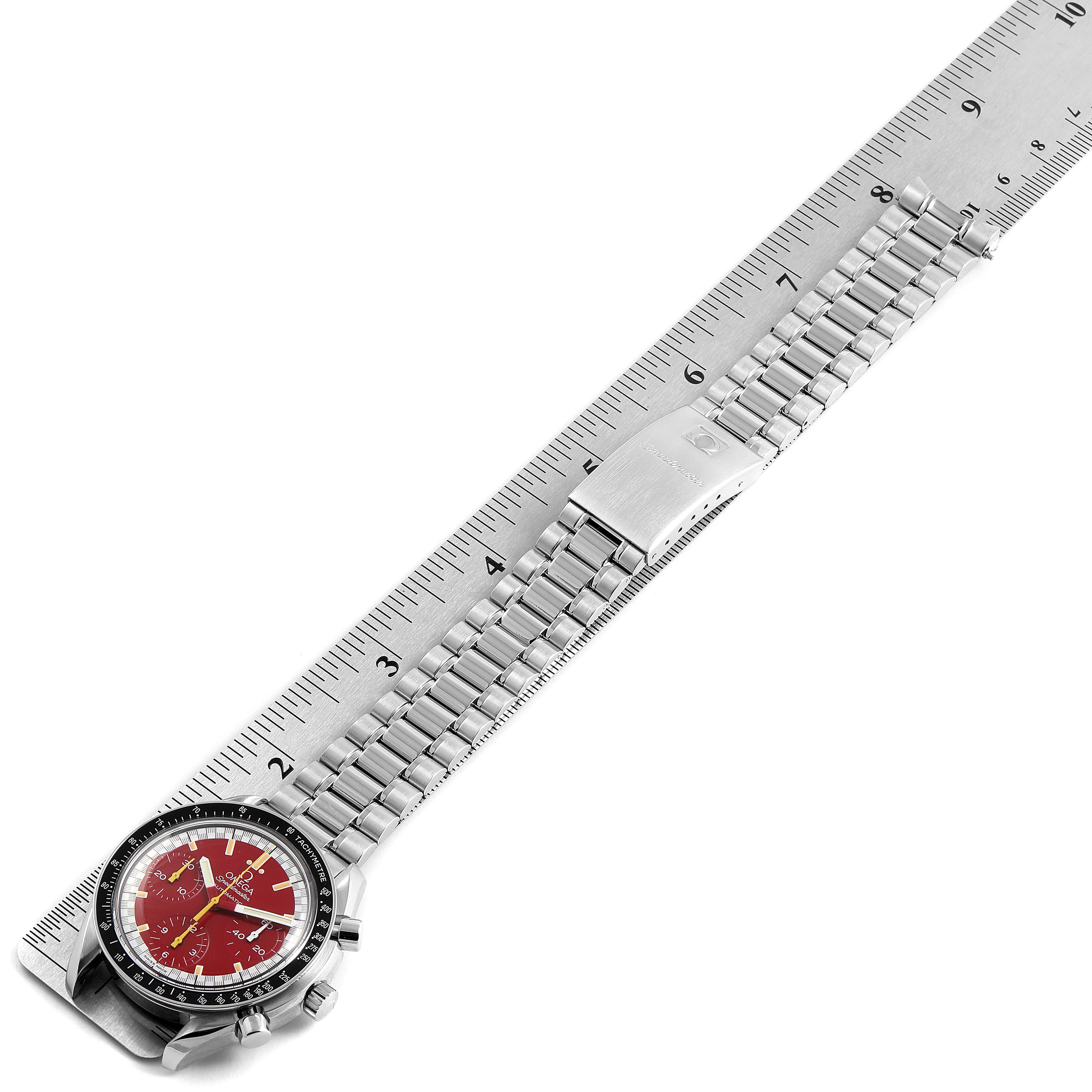 This image shows an Omega Speedmaster 3510.61.00 Men
s Stainless Steel Red Dial 3510.61.00 Men
s Stainless Steel Red Dial watch laid flat on a ruler, displaying its face, bezel, buttons, and metal bracelet.