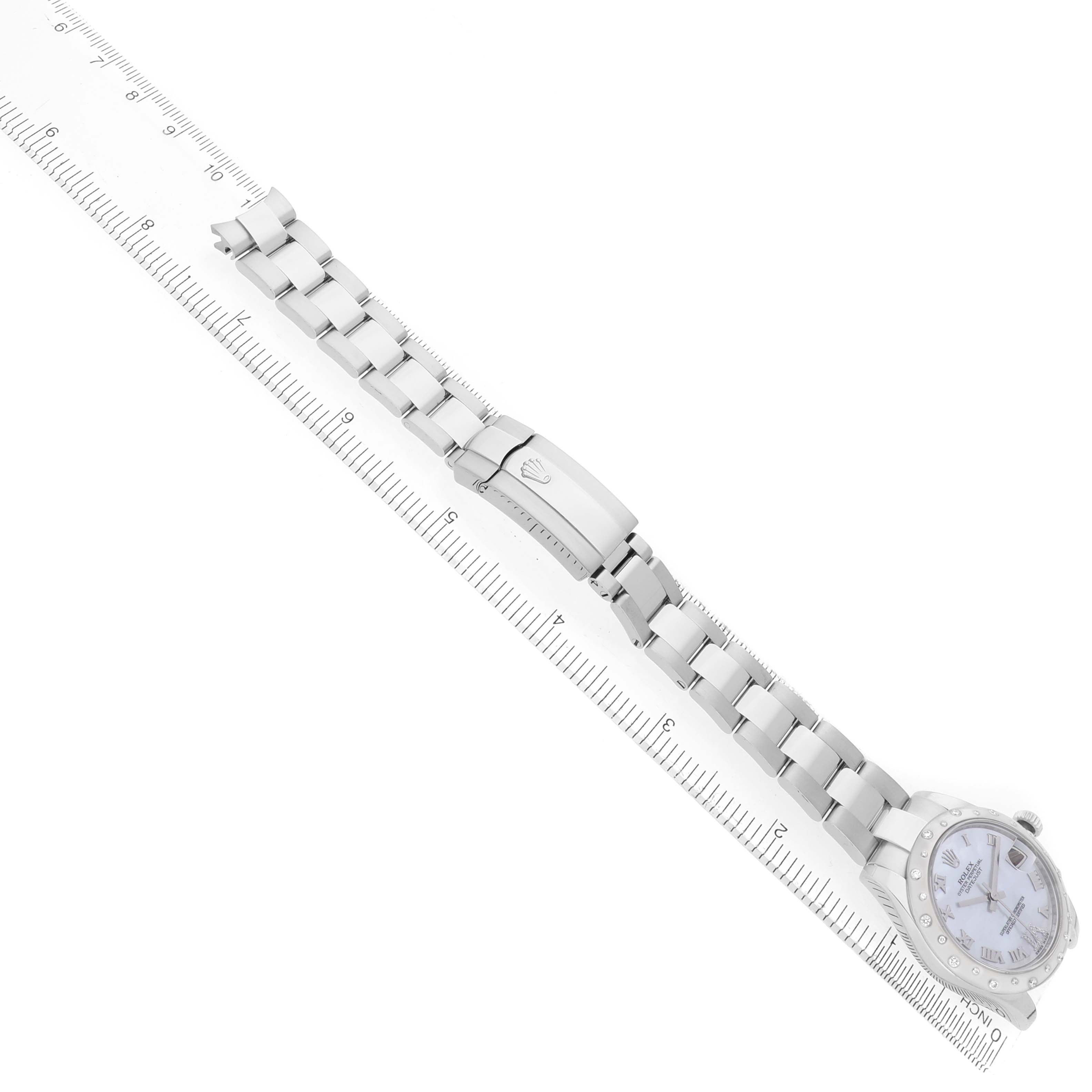 The image shows a Rolex Mid-Size 178344 Women
s Stainless Steel Mother of Pearl Dial watch laid flat alongside a ruler, highlighting the bracelet and face.