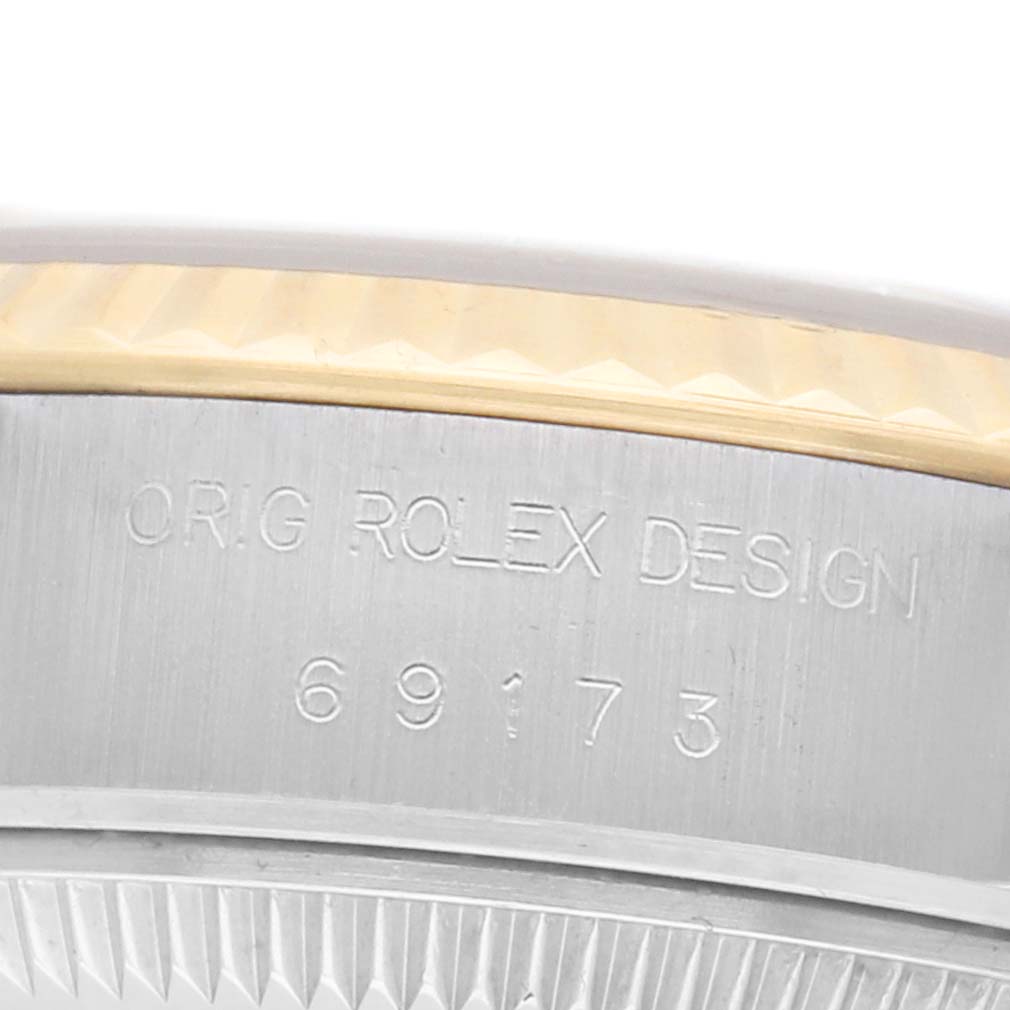 The image shows a close-up of the side of a Rolex Datejust 69173 Women
s Steel and Gold (two tone) Champagne Dial, featuring the bezel and engraved case details.