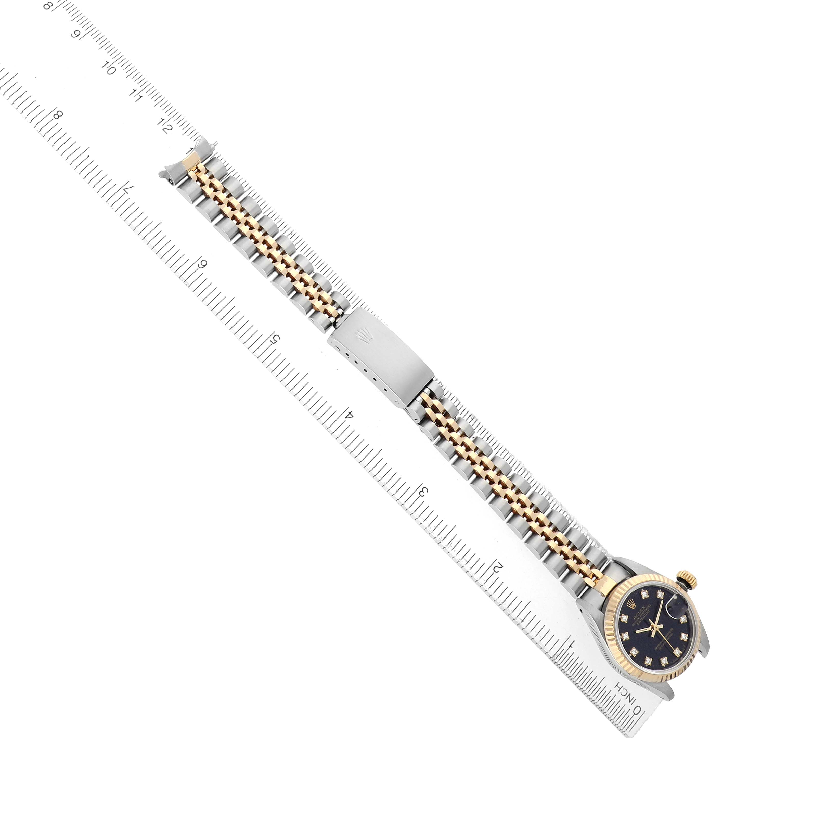 The Rolex Datejust 69173 Women
s Steel and Gold (two tone) Black Dial watch is shown at an angle, highlighting its face, bracelet, and clasp with a ruler for scale.