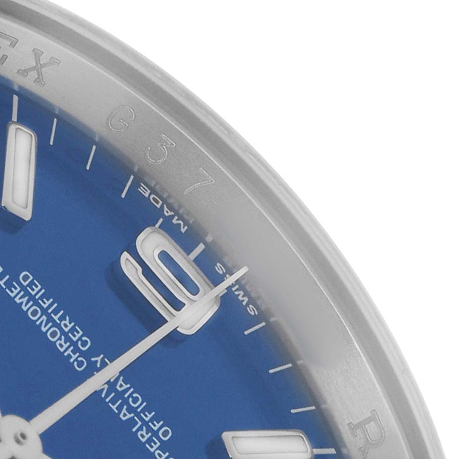 The image shows a partial view of the dial and bezel of a Rolex Oyster Perpetual 116000 Men
s Stainless Steel Blue Dial watch, highlighting the blue dial and hour markers.