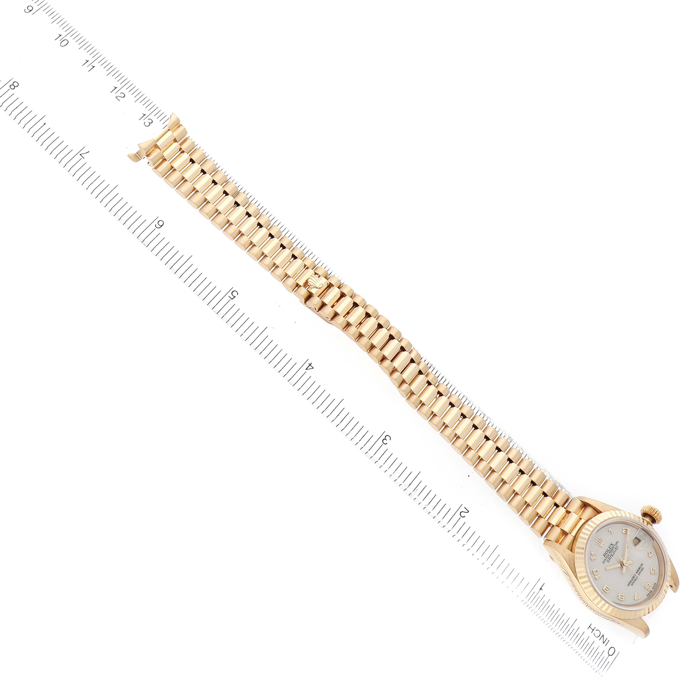 The Rolex President 69178 Women
s Yellow Gold White Dial watch is shown diagonally from an overhead angle, displaying its full bracelet and watch face alongside a ruler.