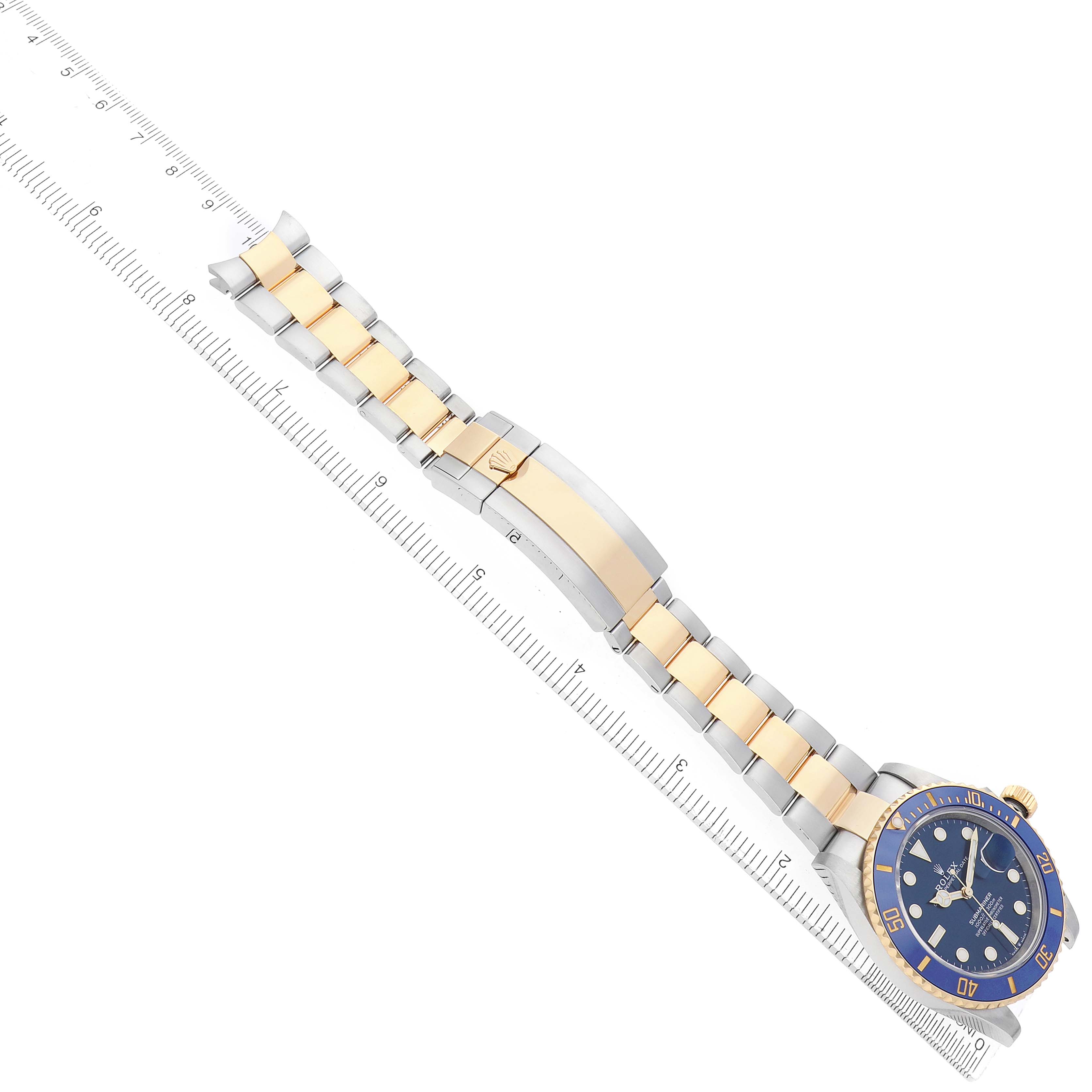 The Rolex Submariner 126613 Men
s Steel and Gold (two tone) Blue Dial is shown flat from a top view, highlighting the bracelet and clasp, alongside a ruler for scale.