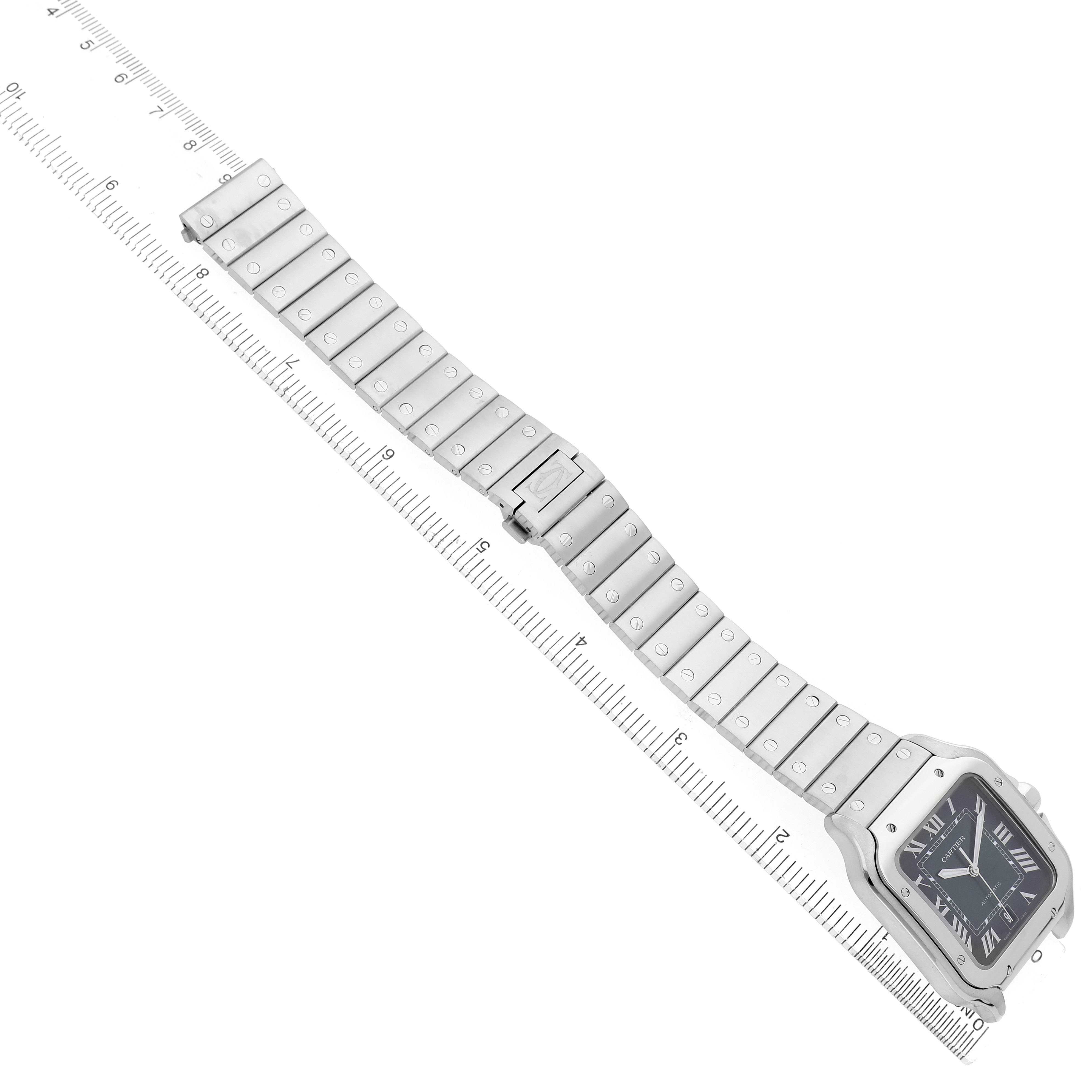 The image shows a Cartier Santos WSSA0062 Men's Stainless Steel Green Dial watch at an angle, highlighting its square face, metal bracelet, and visible clasp on a measurement guide.