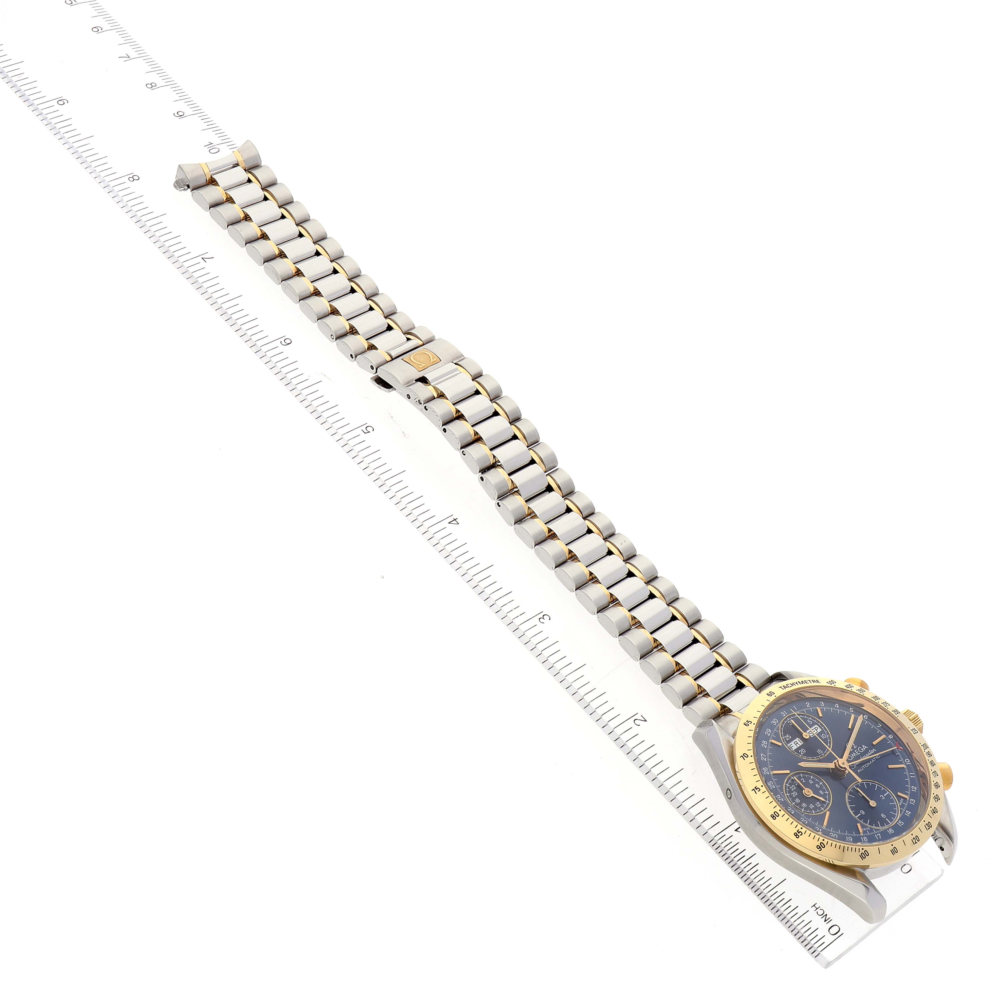 This image shows an Omega Speedmaster 3321.80.00 Men's Steel and Gold (two tone) Blue Dial 3321.80.00 Men's Steel and Gold (two tone) Blue Dial watch laid flat next to a ruler, highlighting the band and face of the watch.
