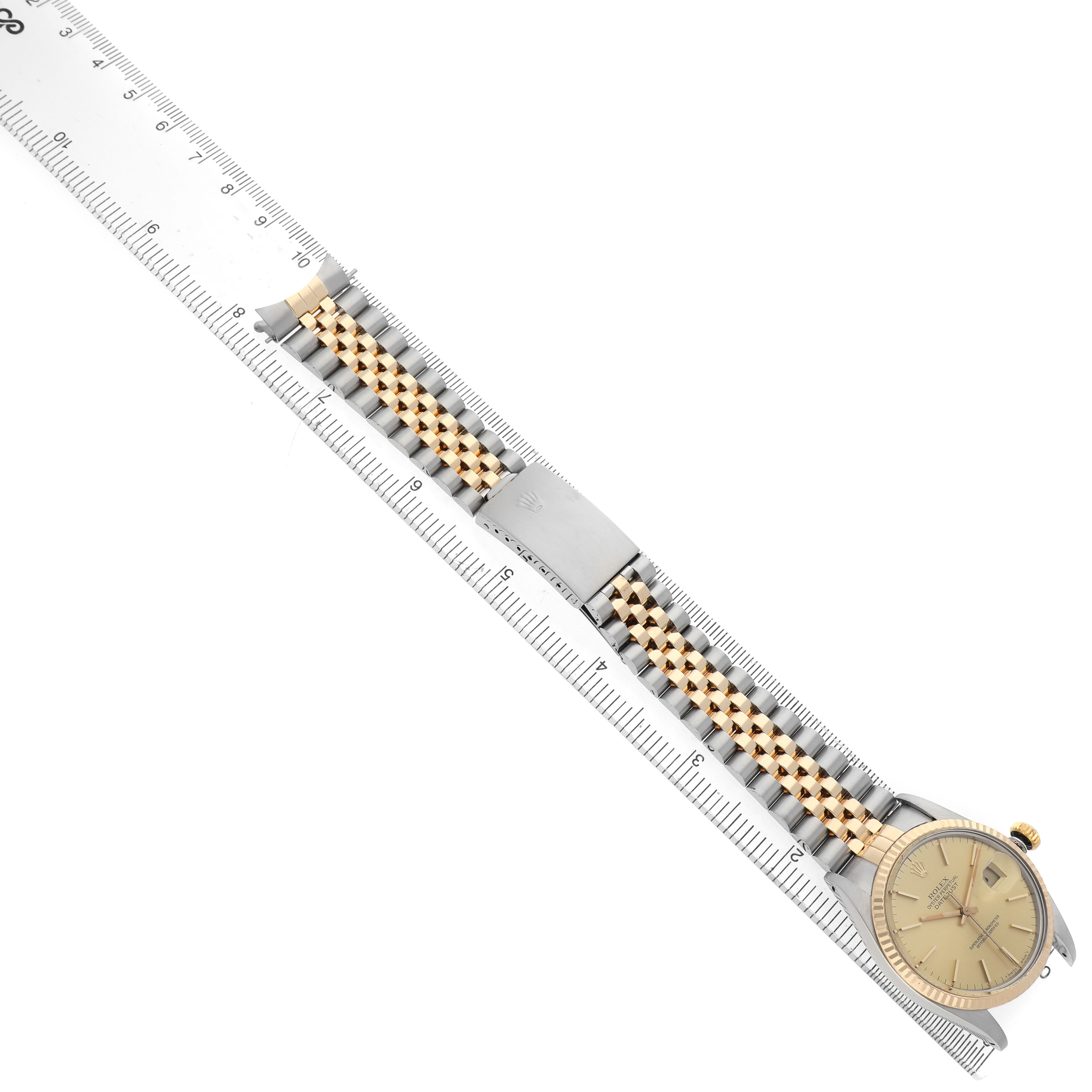 The Rolex Datejust 16013 Men's Stainless Steel Champagne Dial watch is shown at an oblique angle, featuring its face, bracelet, and clasp alongside a measuring ruler.