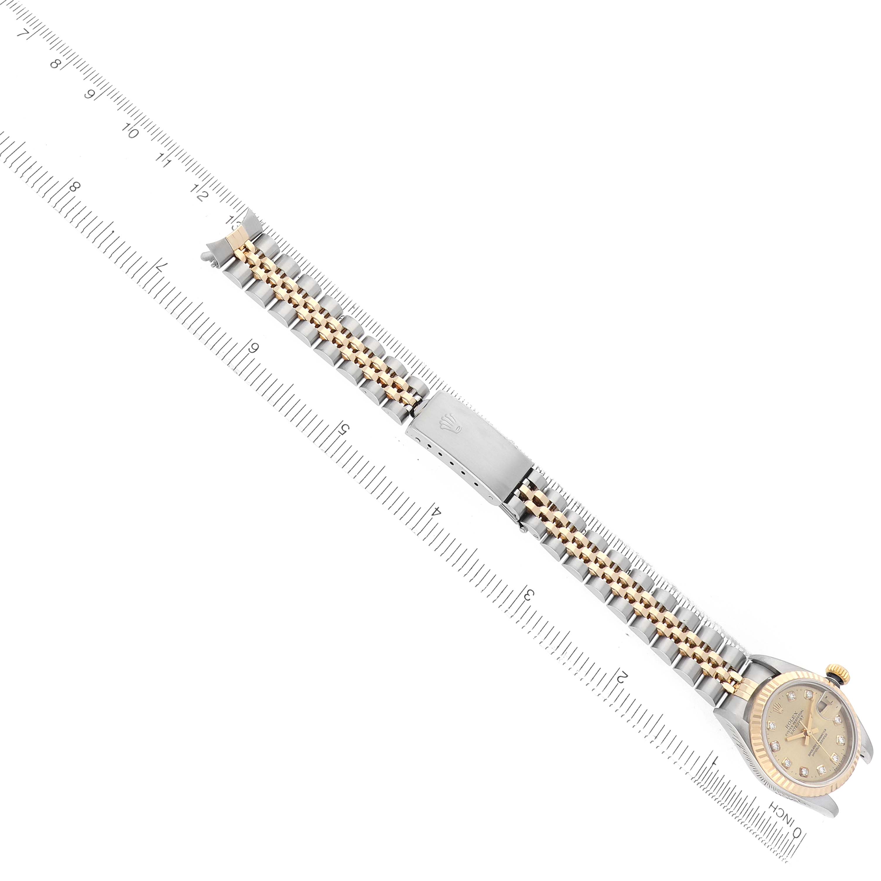 The Rolex Datejust 79173 Women
s Steel and Gold (two tone) Champagne Dial watch is shown from a top-down angle, displaying the face, bezel, and full bracelet alongside a ruler.