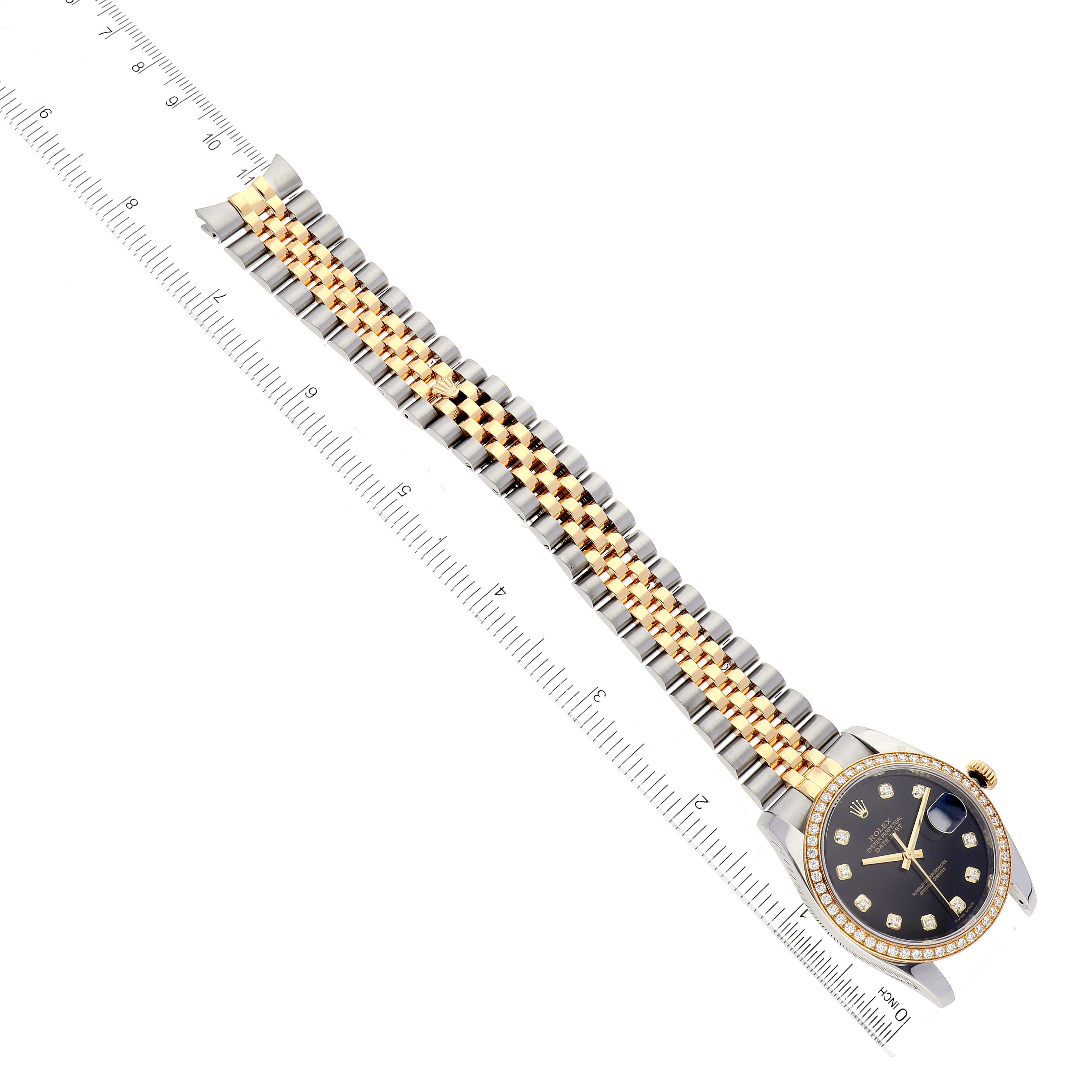 The Rolex Datejust 116243 Men's Steel and Gold (two tone) Black Dial 116243 Men's Steel and Gold (two tone) Black Dial watch is shown from a top-down angle, displaying its face, bracelet, and a ruler for scale.