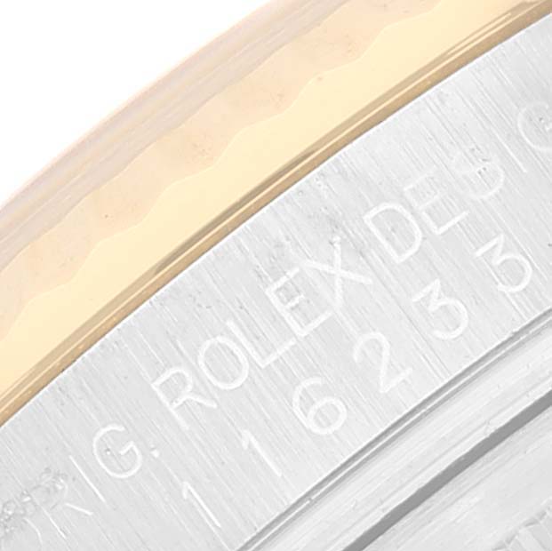 This close-up image of a Rolex Datejust 116233 Men's Steel and Gold (two tone) White Dial 116233 Men's Steel and Gold (two tone) White Dial watch shows part of the watch bezel and the edge with engraved text.
