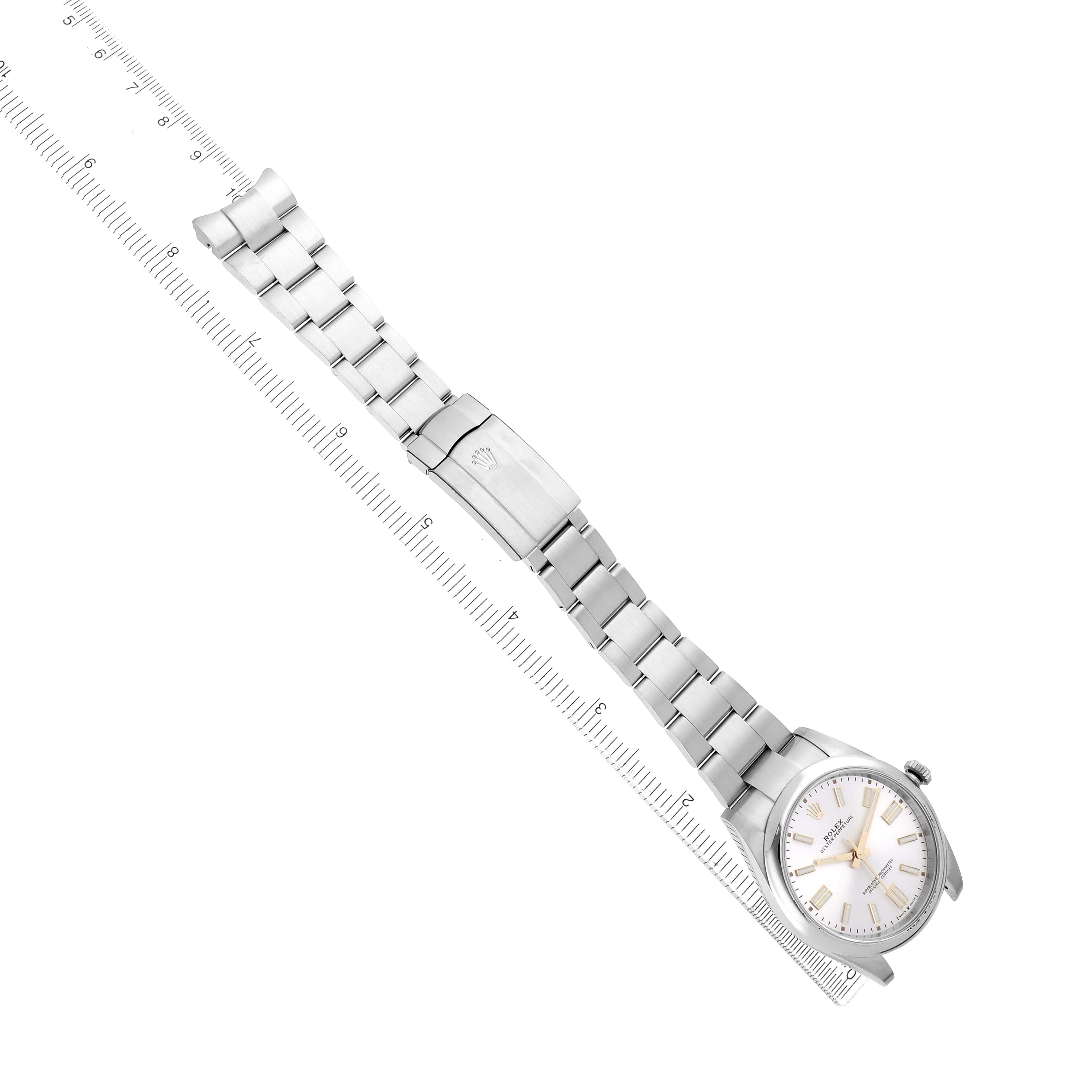 The image shows a Rolex Oyster Perpetual 124300 Men
s Stainless Steel Silver Dial watch at an angled view, displaying the dial, bracelet, and clasp alongside a measuring ruler.