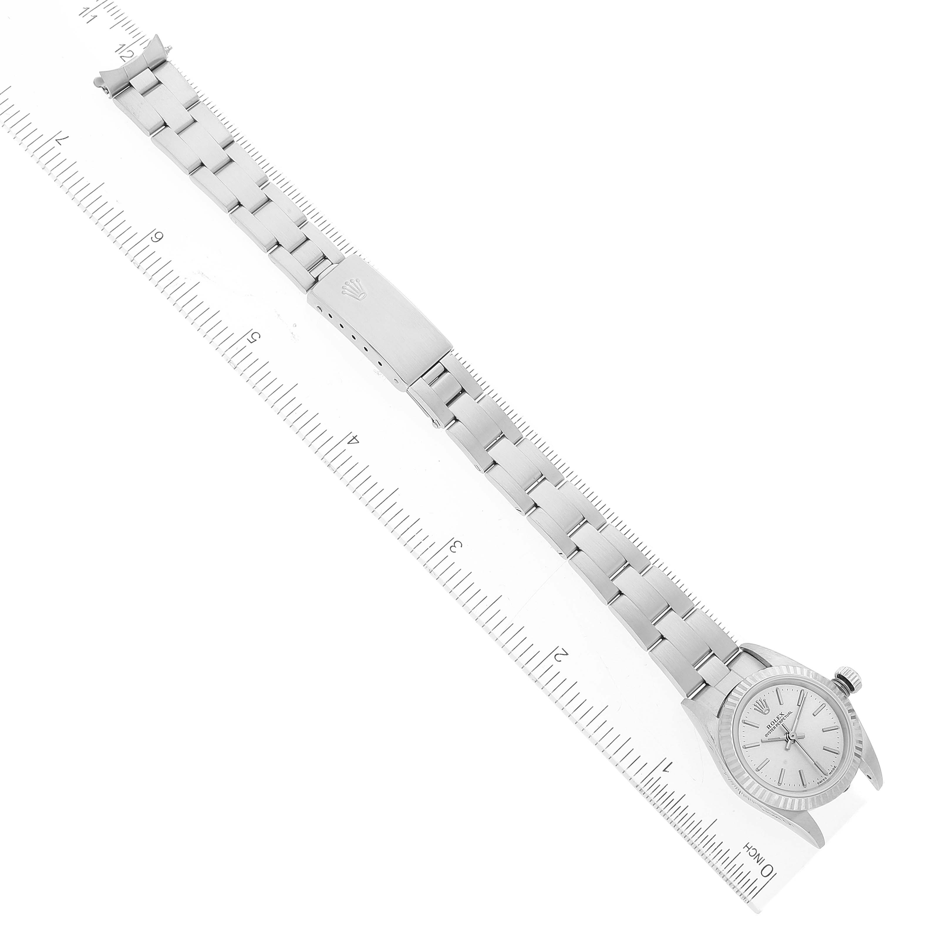 The image shows the Rolex Oyster Perpetual 76094 Women's Stainless Steel Silver Dial 76094 Women's Stainless Steel Silver Dial watch with its full metal bracelet laid parallel to a ruler, viewed from above.