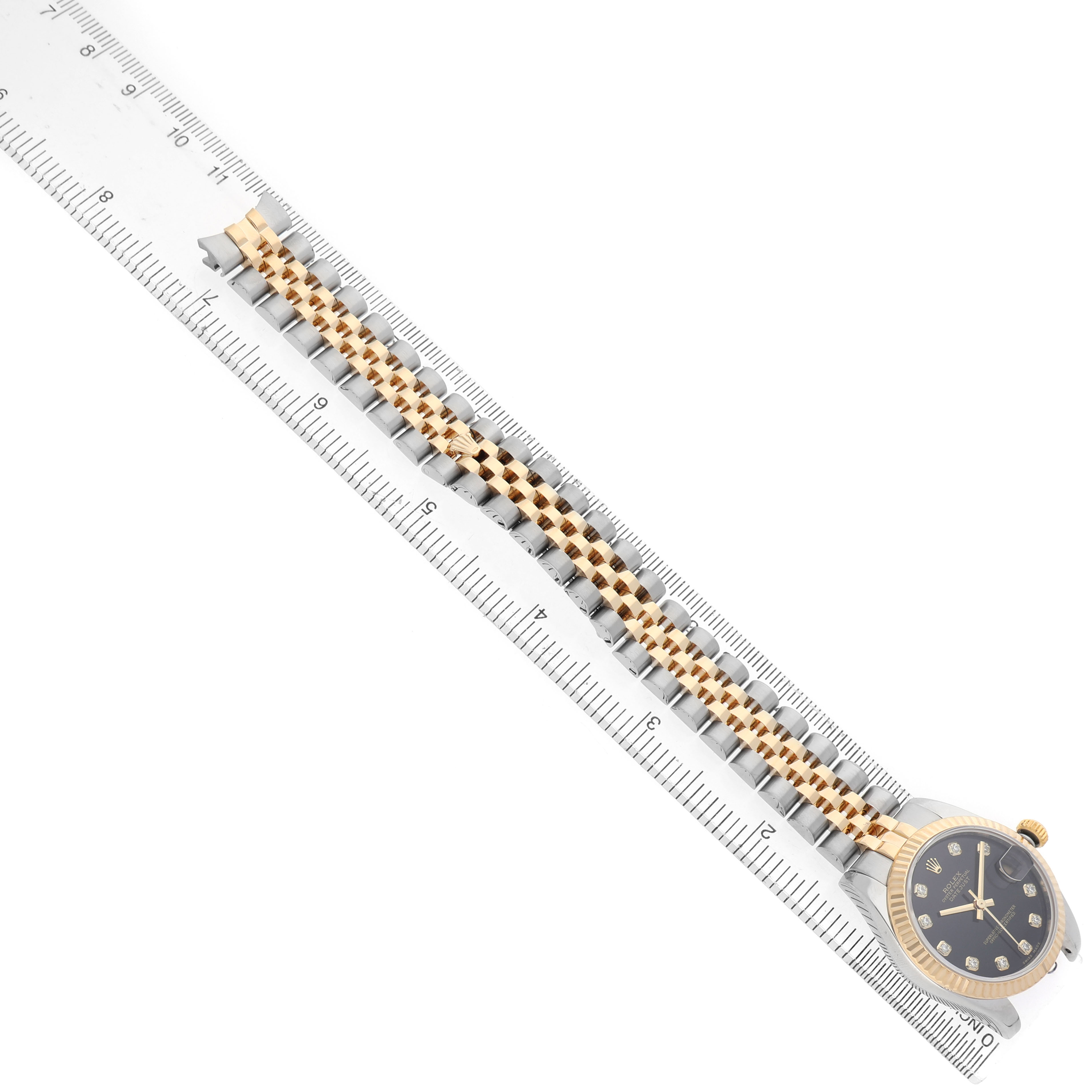 The Rolex Datejust 178273 Women's Steel and Gold (two tone) Black Dial watch is shown diagonally with its bracelet and face alongside a ruler for scale.