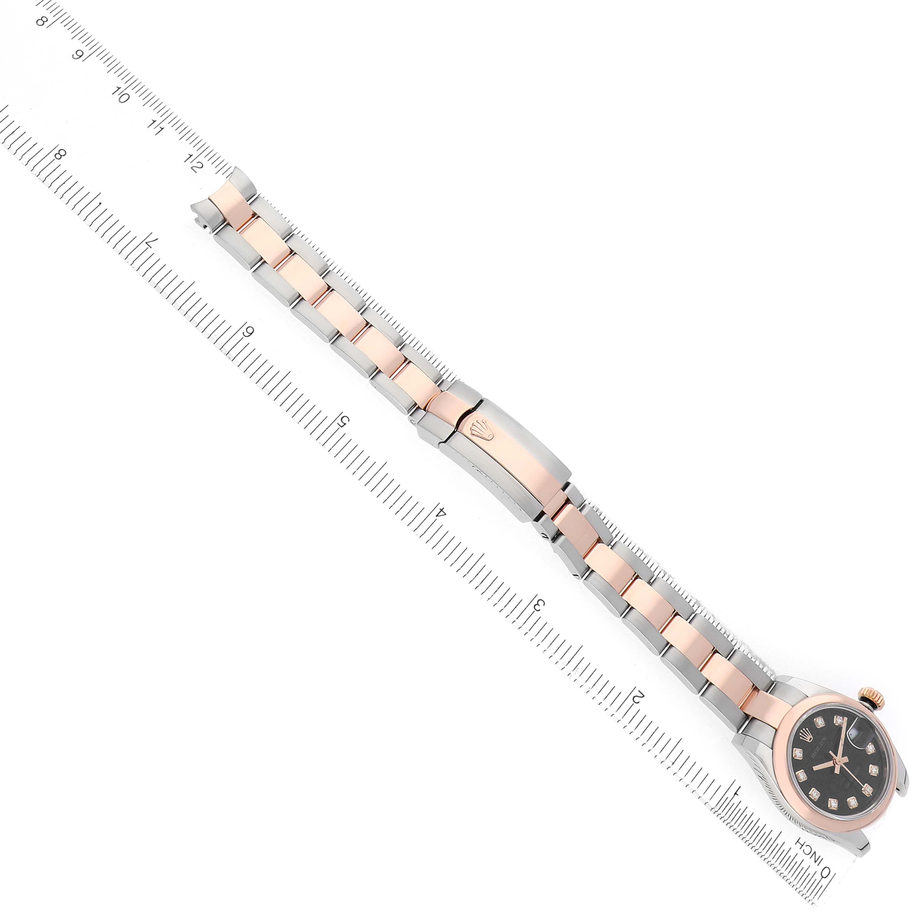 The Rolex Datejust 179161 Women
s Steel and Gold (two tone) Black Dial watch is shown from an angled top view, displaying the face, metal bracelet, and clasp beside a ruler.