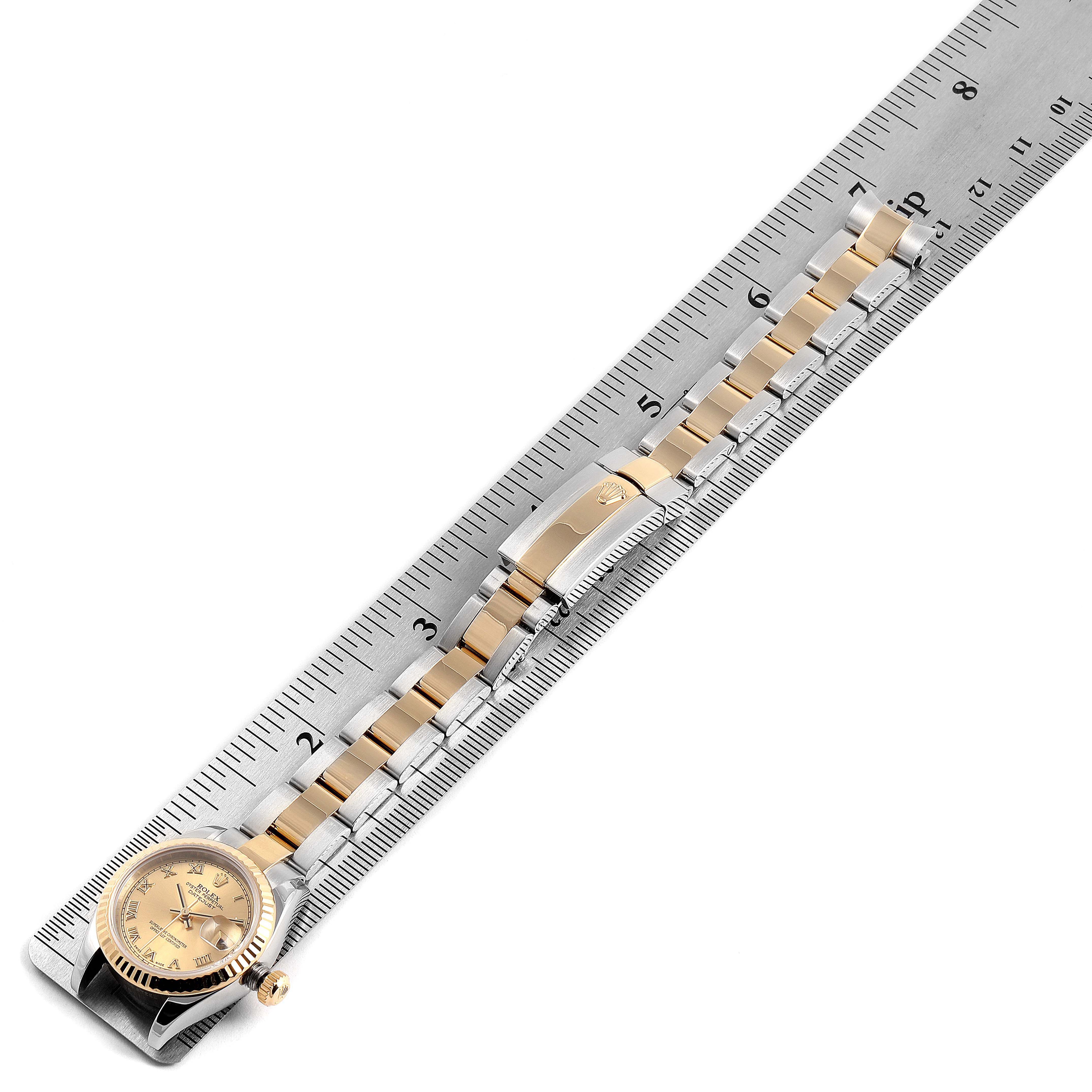 This image shows a Rolex Datejust 179173 Women's Steel and Gold (two tone) Champagne Dial 179173 Women's Steel and Gold (two tone) Champagne Dial watch laid flat next to a ruler, highlighting the watch face, bracelet, and clasp.