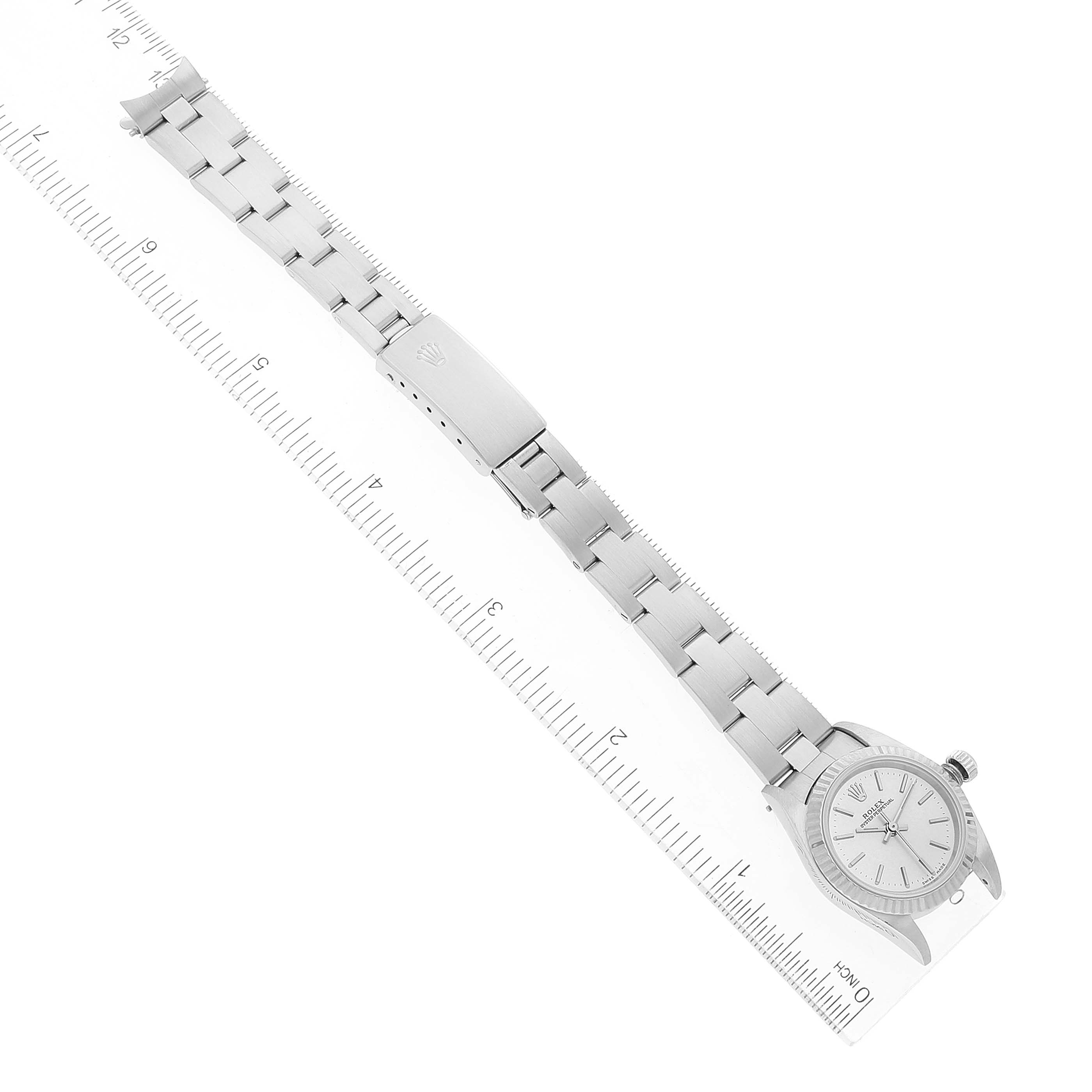 The image shows an overhead view of a Rolex Oyster Perpetual 76094 Women
s Stainless Steel Silver Dial 76094 Women
s Stainless Steel Silver Dial watch with its full stainless steel bracelet against a ruler.