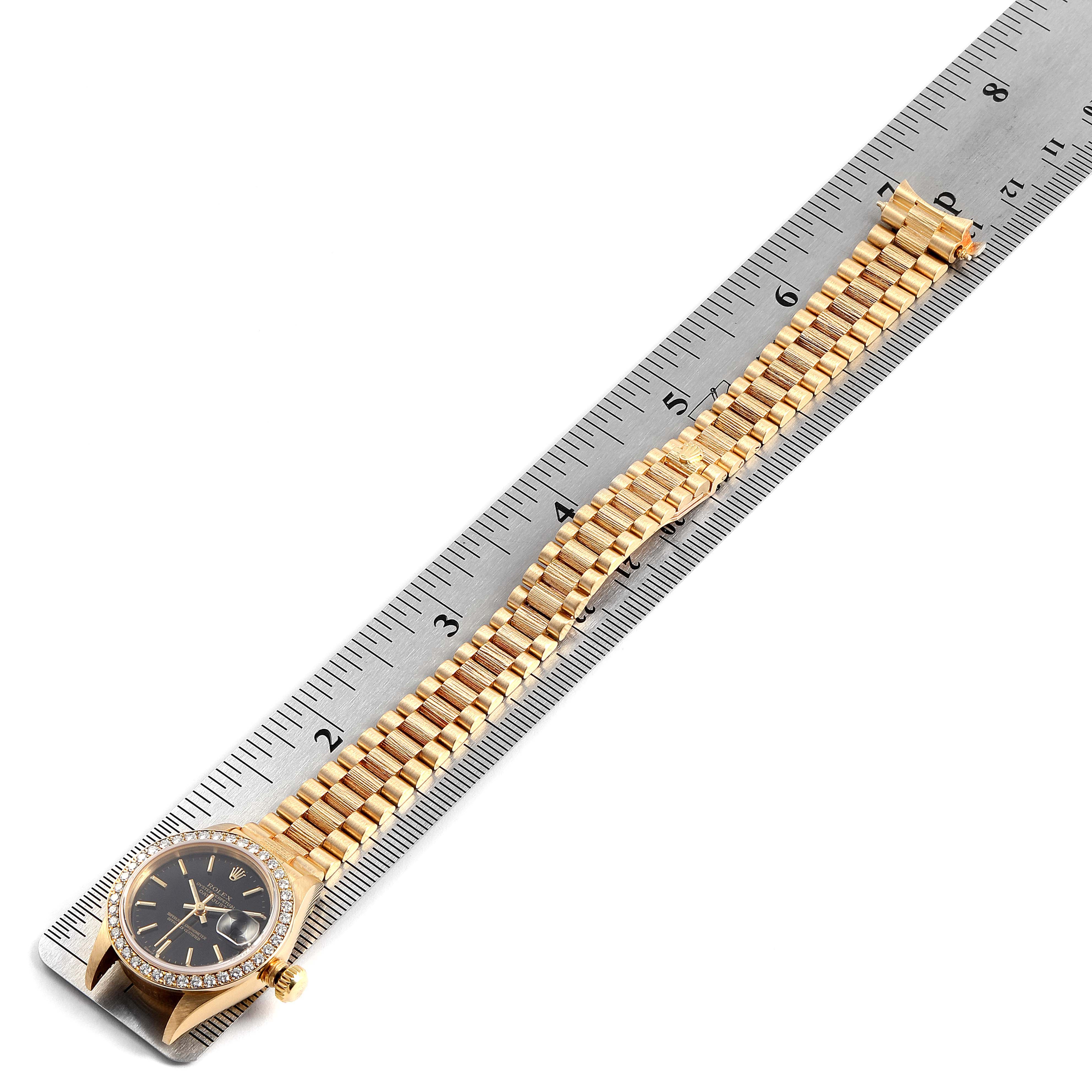 The image shows a Rolex President 69288 Men
s Yellow Gold Black Dial 69288 Men
s Yellow Gold Black Dial model watch, top view, featuring its face, bezel, and full linked bracelet along a ruler.