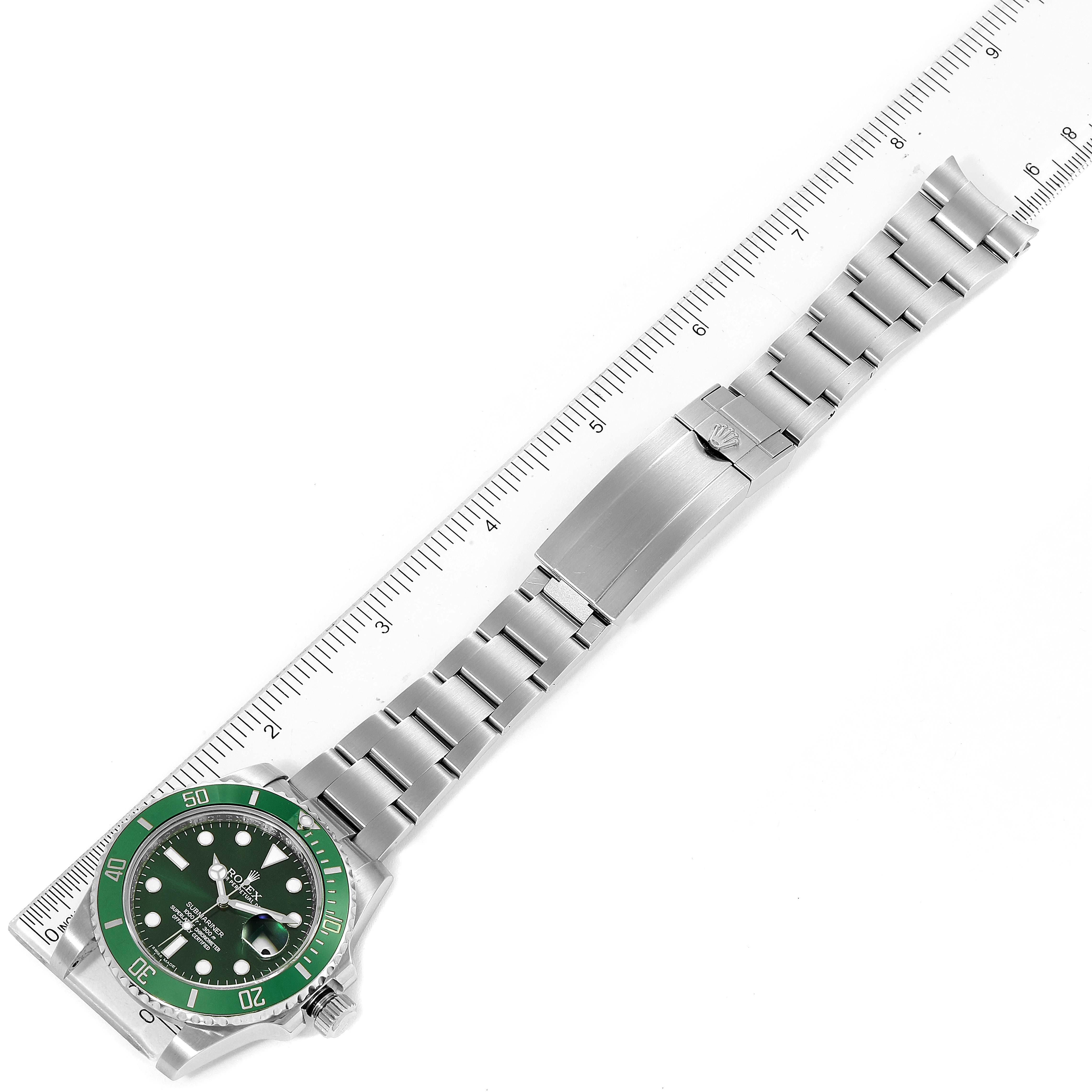 The Rolex Submariner 116610LV Men's Stainless Steel Green Dial 116610LV Men's Stainless Steel Green Dial watch is shown from a top-down angle, displaying its green bezel, dial, and stainless steel bracelet beside a ruler.