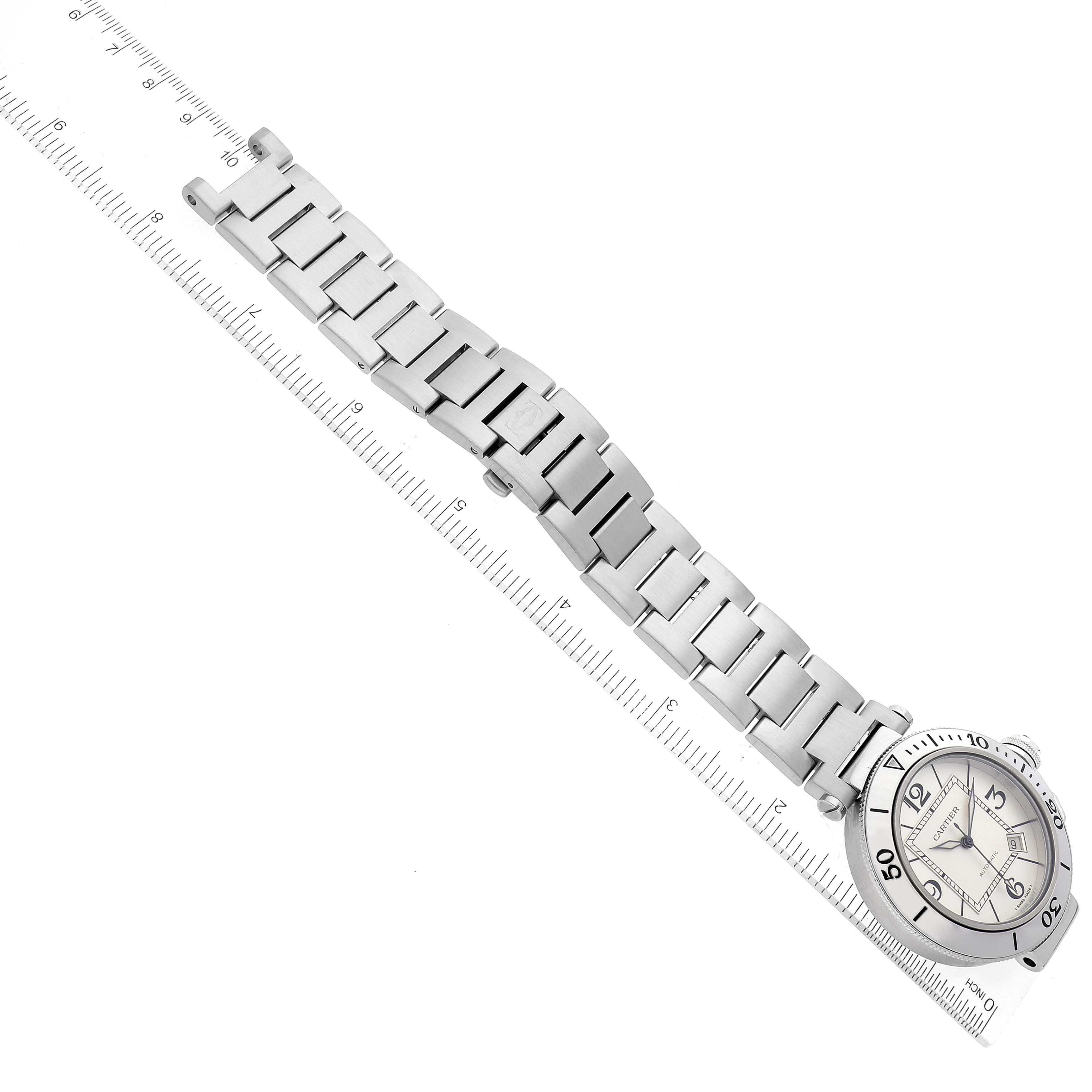 The image shows a flat, top-down view of a Pasha model by Cartier, highlighting the watch face and metal bracelet against a ruler background.