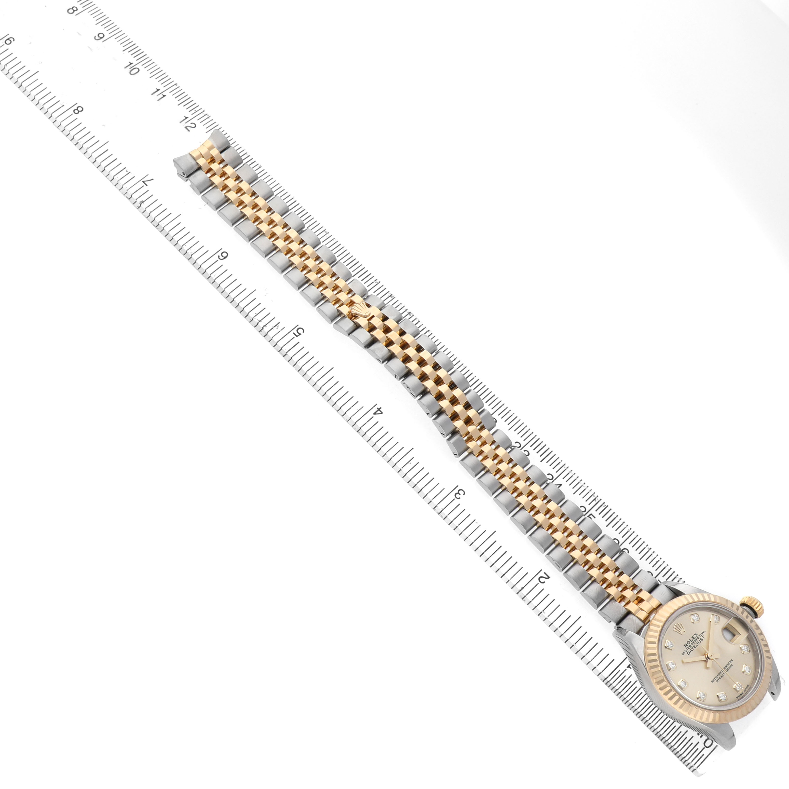 The Rolex Datejust 279173 Women's Stainless Steel Champagne Dial watch is shown from a top-down angle, displaying the dial, bracelet, and part of a measuring ruler.
