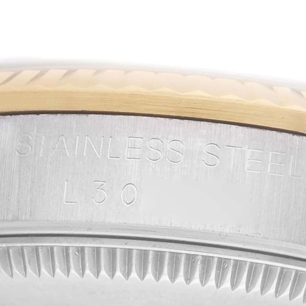 The image shows a close-up of a Rolex Datejust 68273 Women
s Steel and Gold (two tone) Champagne Dial
s stainless steel and gold case side, featuring engravings and a fluted bezel.