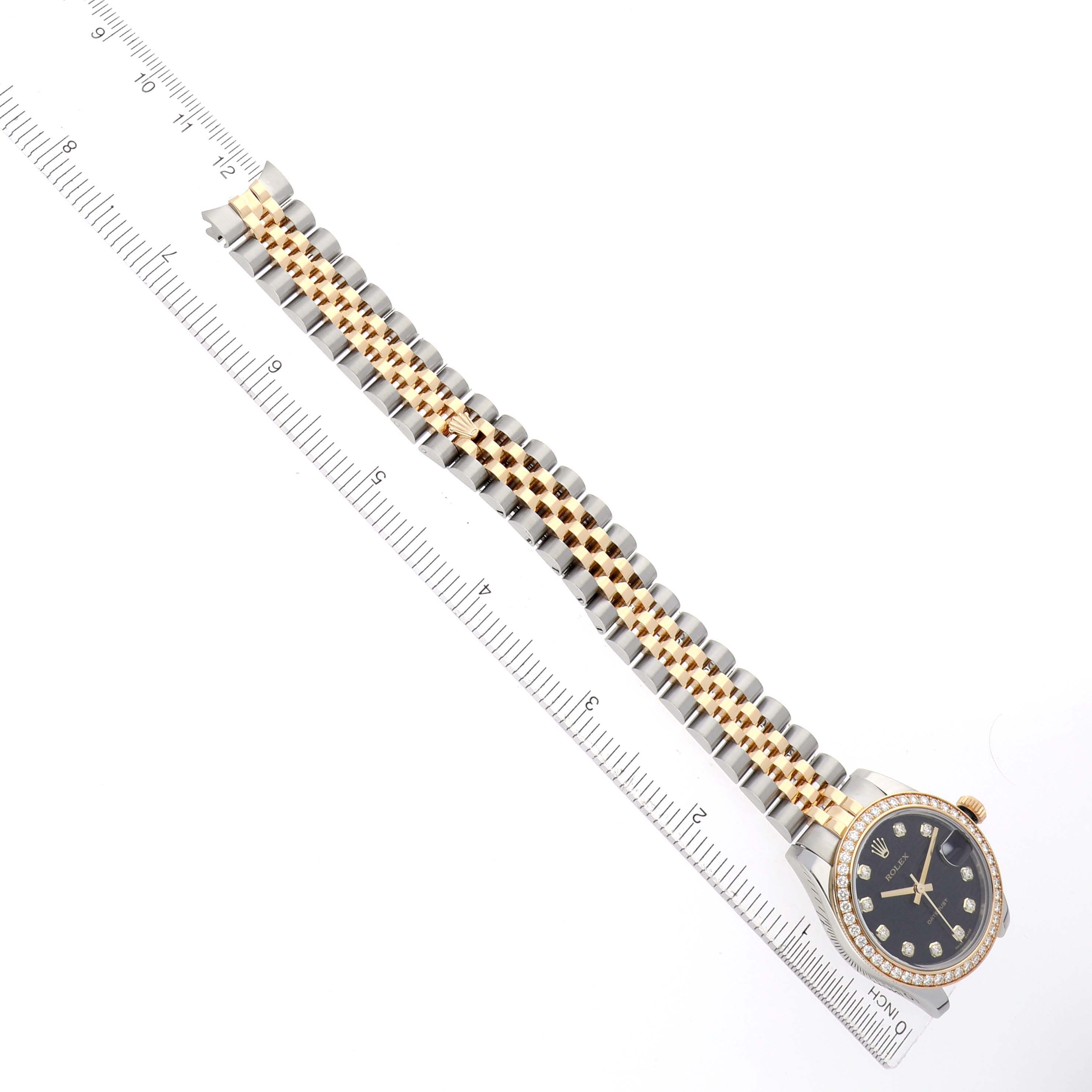 The Rolex Mid-Size 178383 Women
s Steel and Gold (two tone) Black Dial watch is shown at an overhead angle, displaying the face and full bracelet, alongside a ruler for scale.