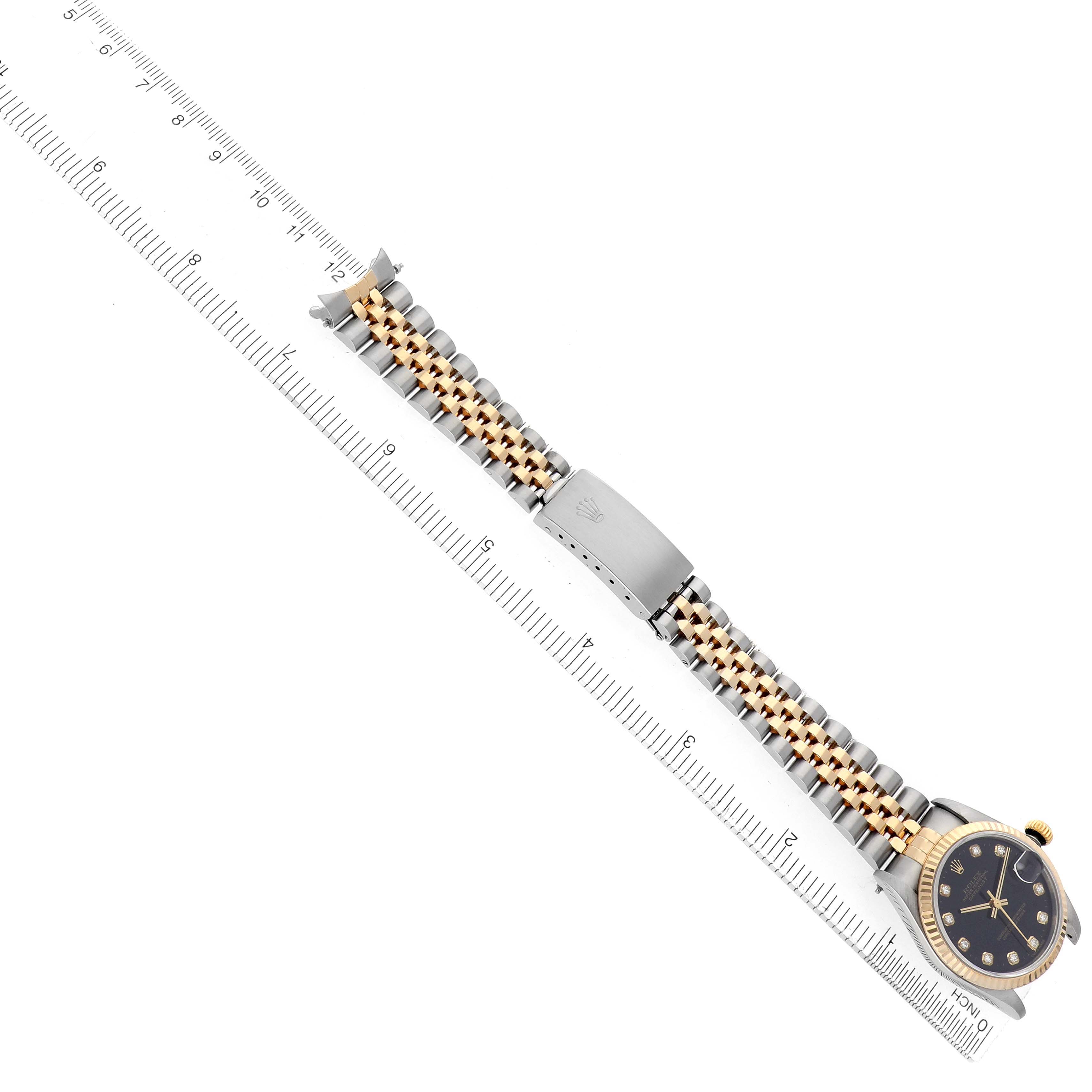 The Rolex Mid-Size 68273 Women
s Steel and Gold (two tone) Black Dial watch is shown from the top, highlighting the face, bracelet, and clasp alongside a ruler for scale.