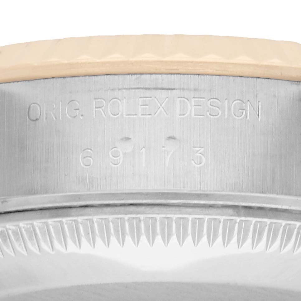 The image shows the side view of a Rolex Datejust 69173 Women
s Steel and Gold (two tone) White Dial model
s case, focusing on the engraved text and bezel details.