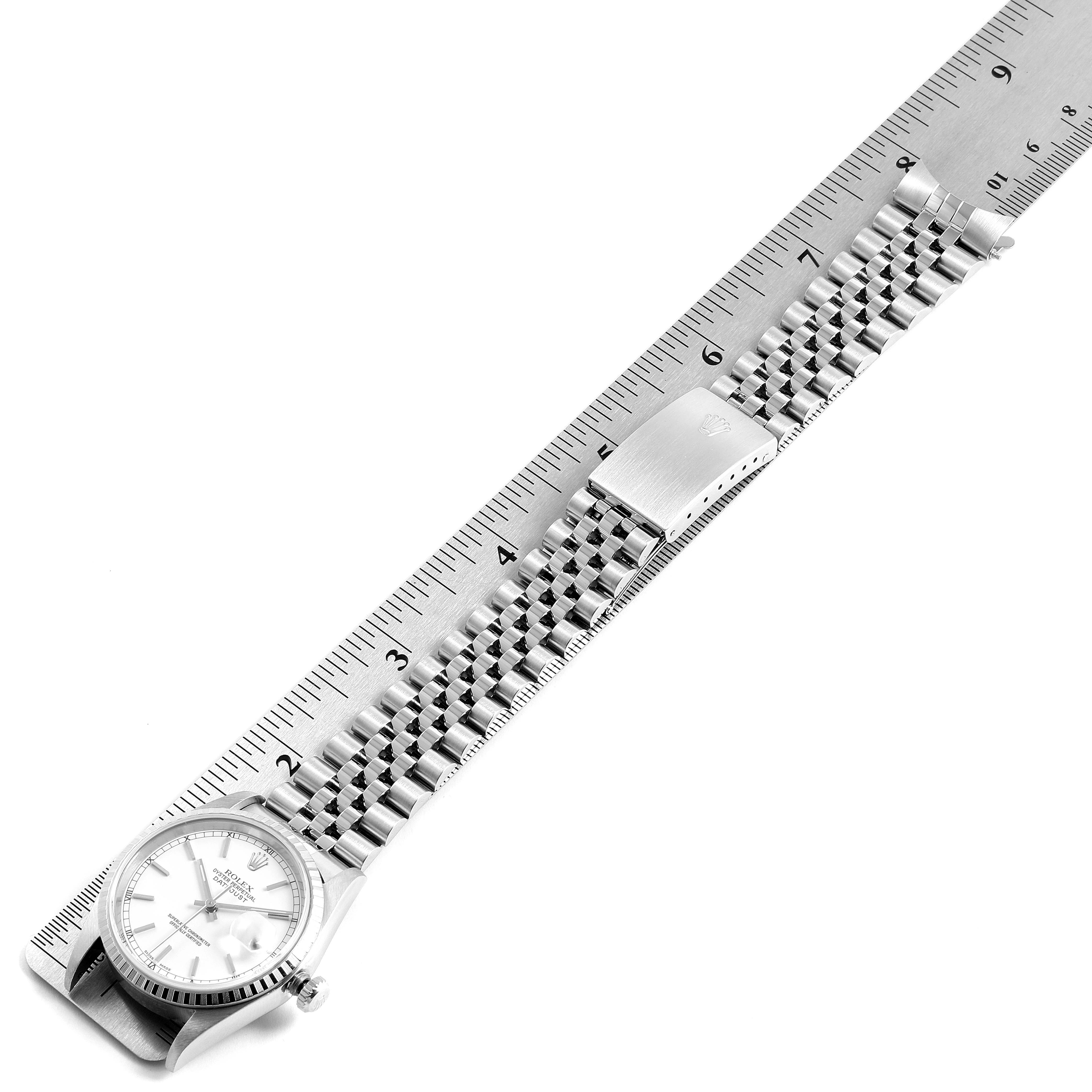 The image shows a Rolex Datejust 16220 Men's Stainless Steel White Dial 16220 Men's Stainless Steel White Dial watch laid flat on a ruler, displaying its face, crown, and bracelet.