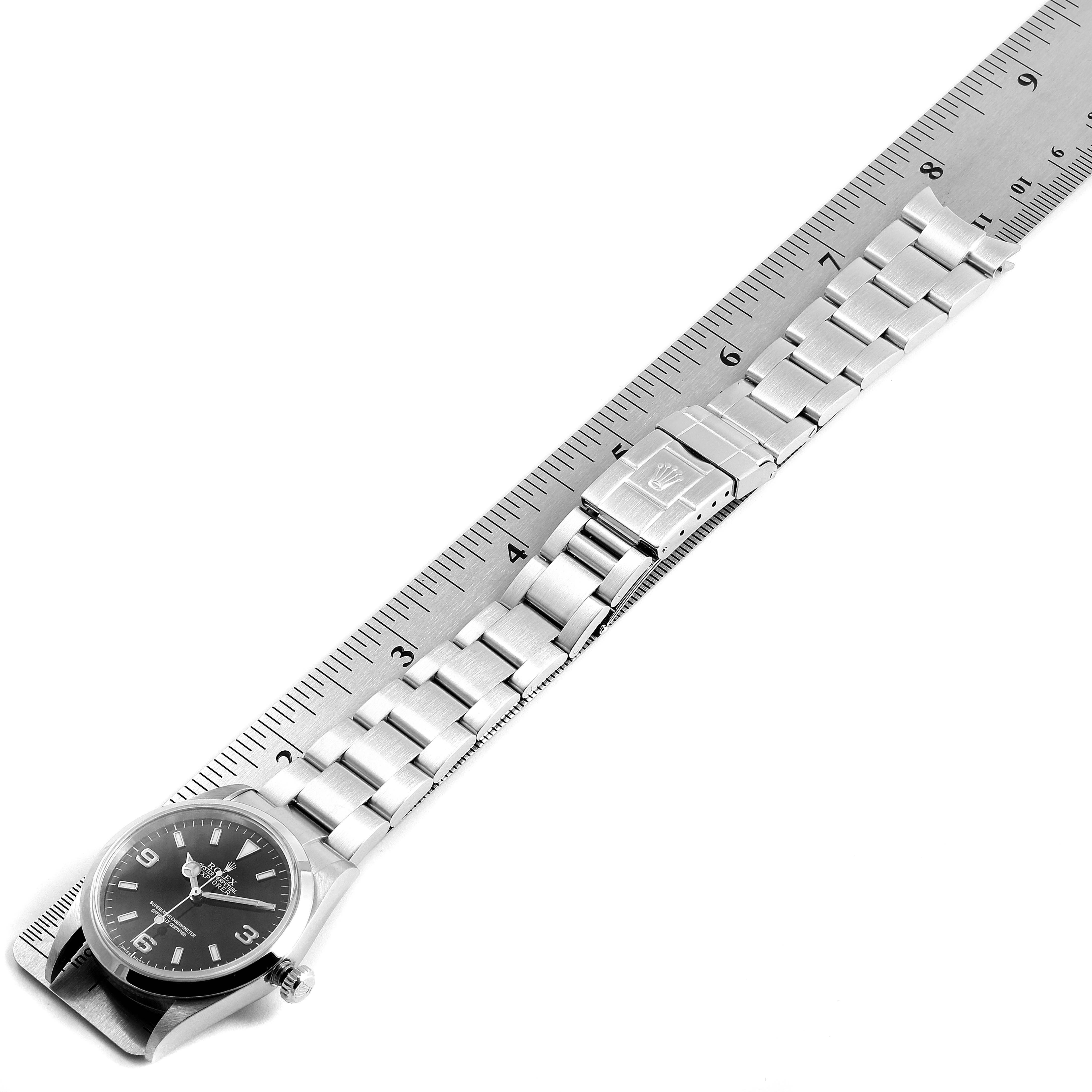 The image shows a side view of a Rolex Explorer 114270 Men
s Stainless Steel Black Dial 114270 Men
s Stainless Steel Black Dial watch, laid flat with a stainless steel bracelet and a measuring ruler beside it.