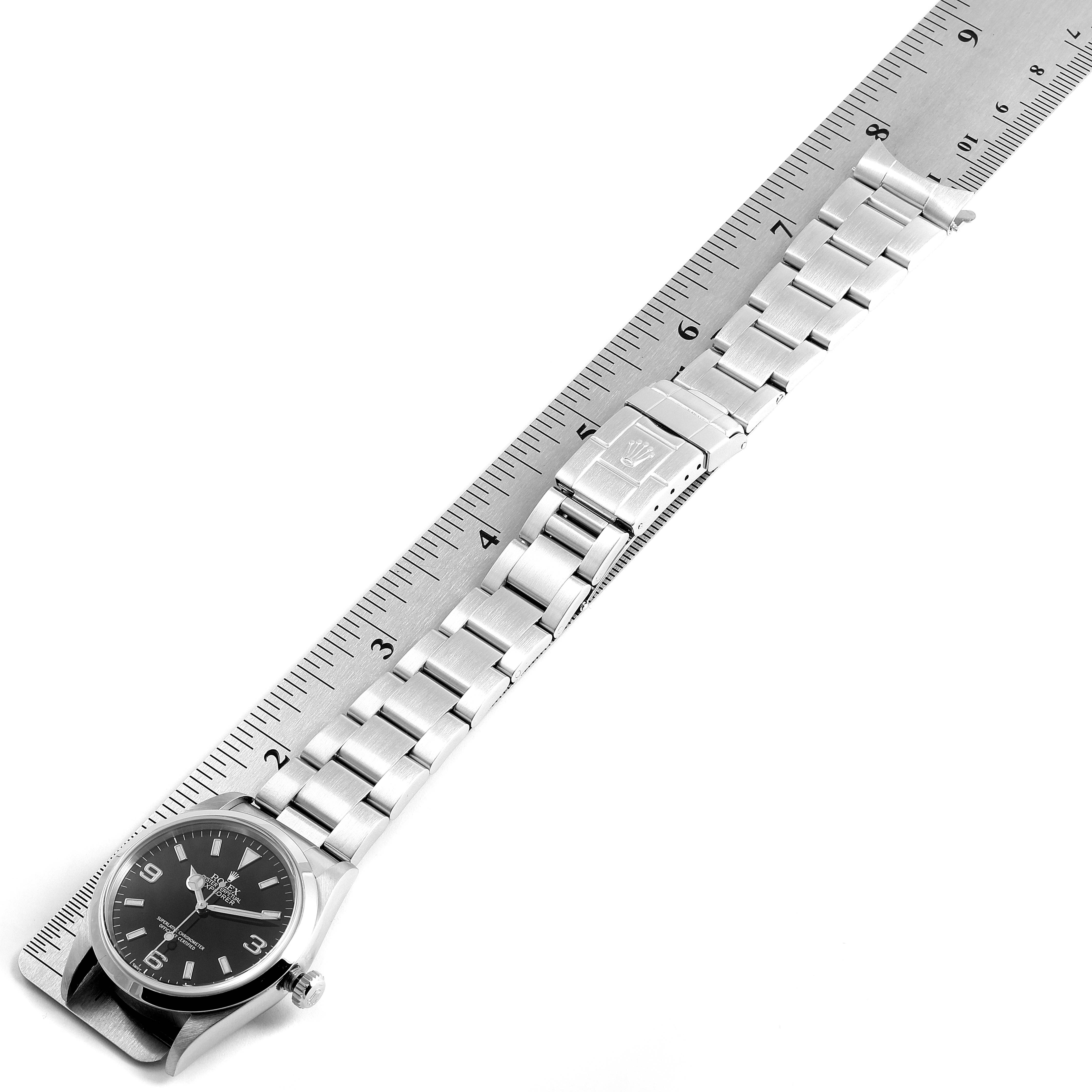 A Rolex Explorer 14270 Men
s Stainless Steel Black Dial 14270 Men
s Stainless Steel Black Dial watch is shown laid flat, showcasing the dial, bracelet, and clasp, measured against a metal ruler.