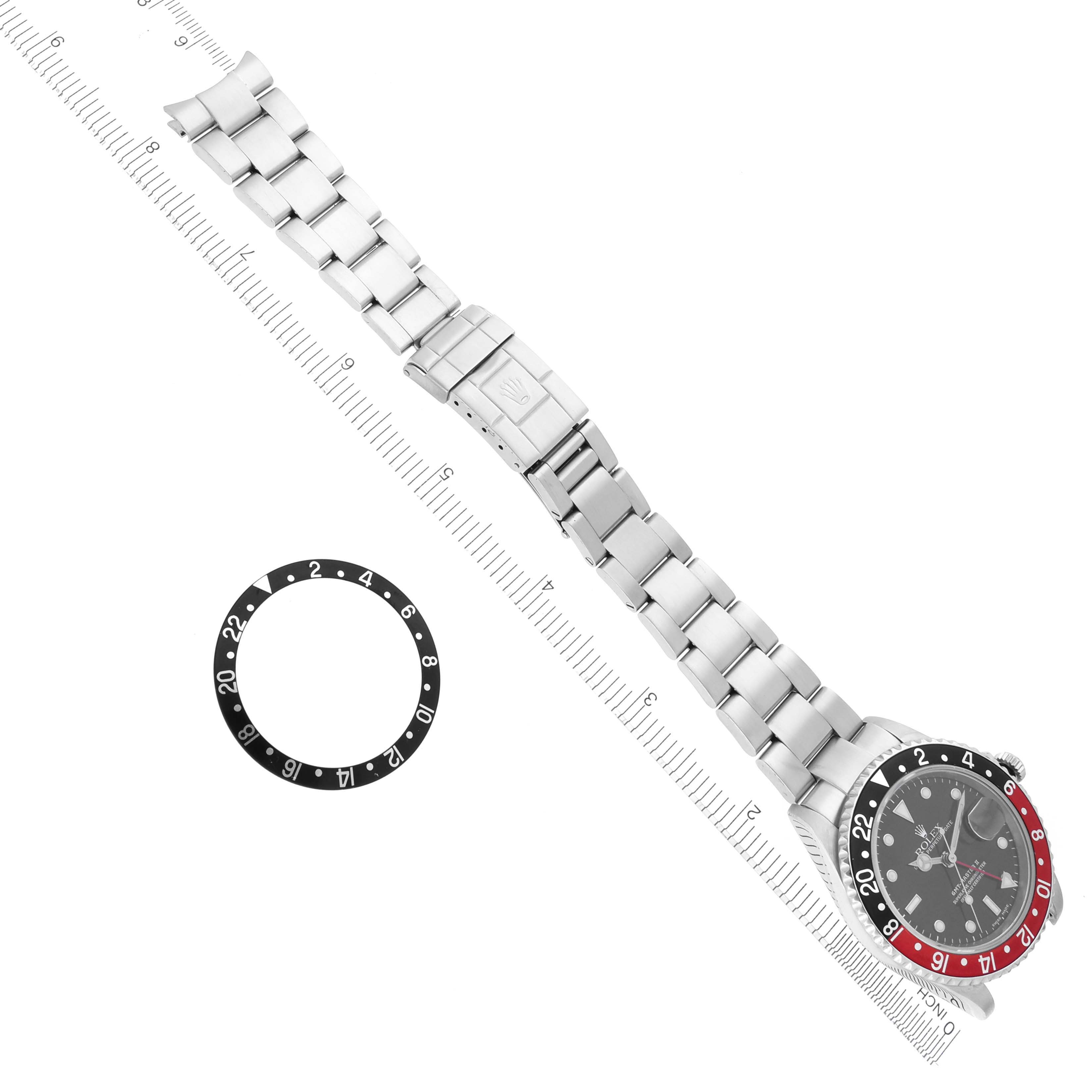 The Rolex GMT-Master 16710 Men
s Stainless Steel Black Dial 16710 Men
s Stainless Steel Black Dial watch is shown from the top, along with a separate bezel inlay, placed alongside a ruler.