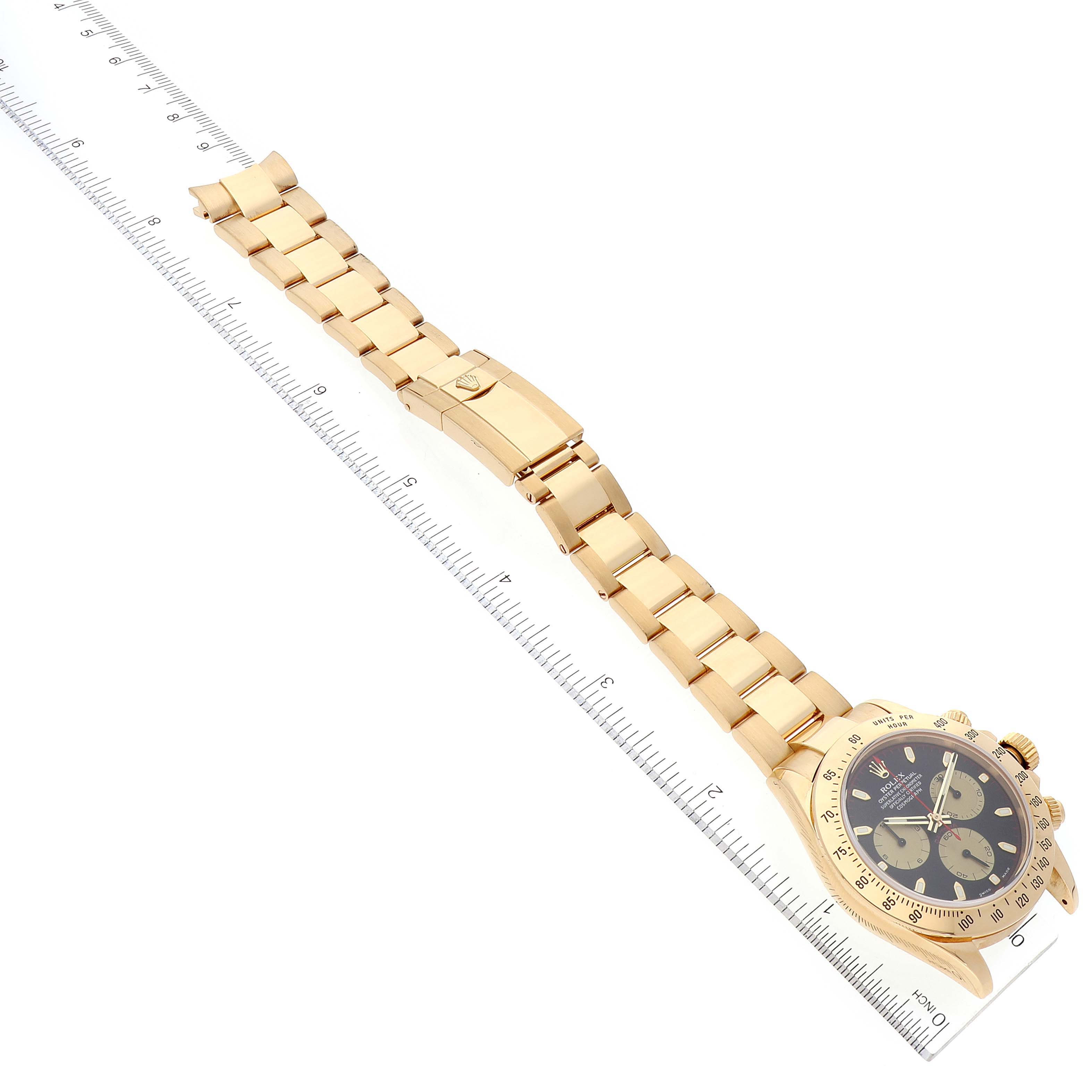 This image shows a Rolex Daytona 116528 Men's Yellow Gold Black Dial 116528 Men's Yellow Gold Black Dial watch laid flat, displaying the full gold-toned band and clasp, and the face placed near a ruler for scale.