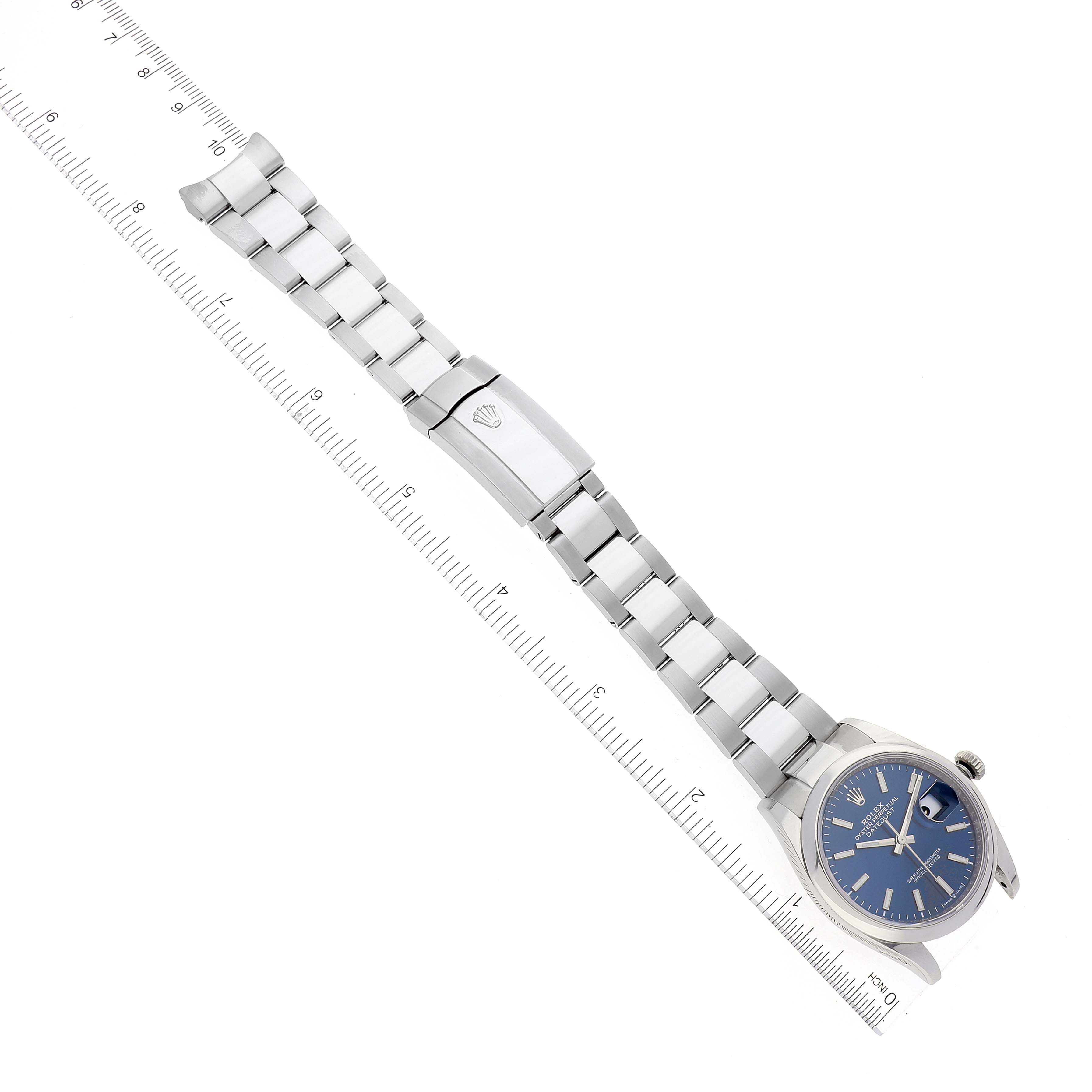 The image shows an overhead view of a Rolex Datejust 126200 Men's Stainless Steel Blue Dial 126200 Men's Stainless Steel Blue Dial watch, focusing on the dial, bracelet, and clasp next to a ruler.