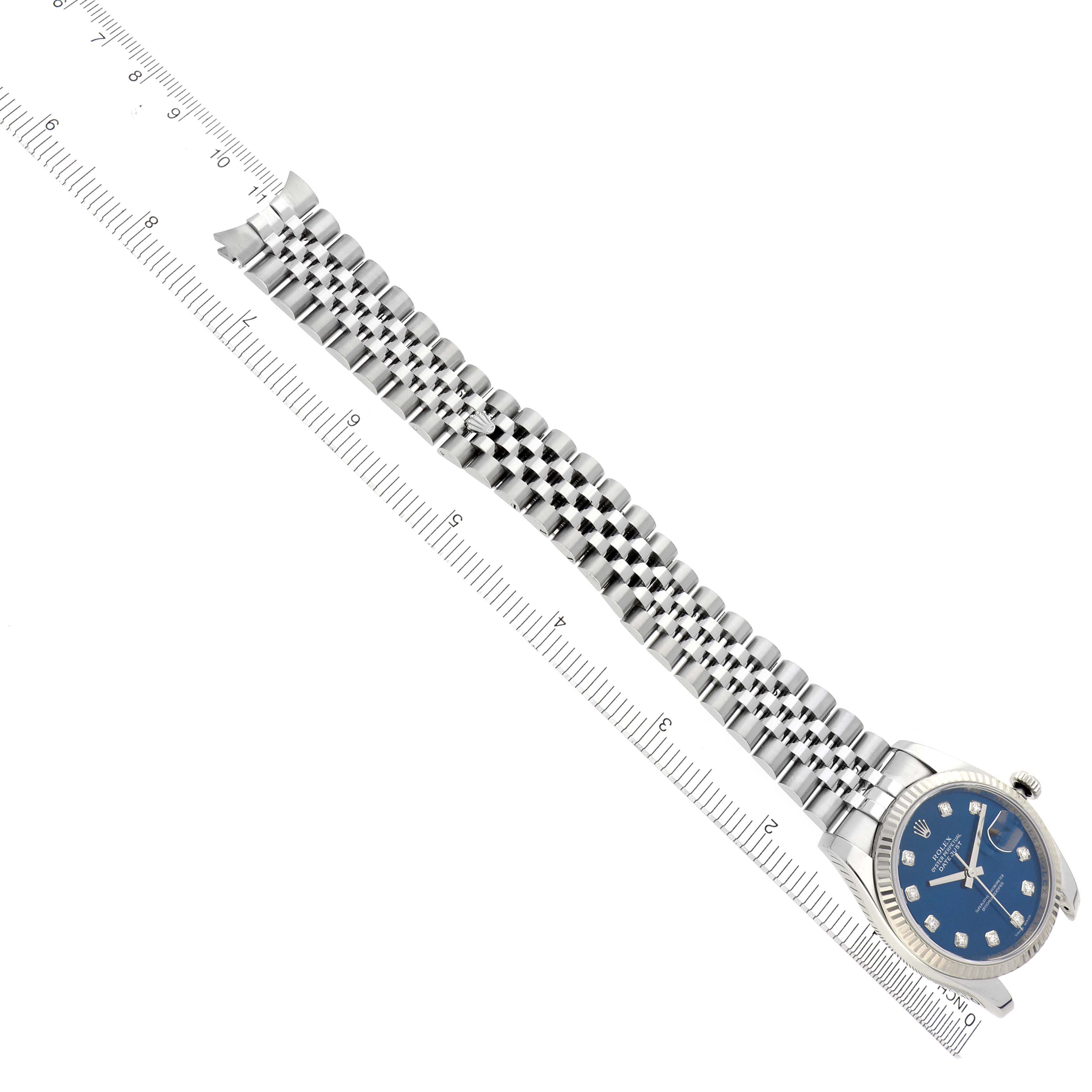 The Rolex Datejust 116234 Men
s Stainless Steel Blue Dial 116234 Men
s Stainless Steel Blue Dial watch is shown from a top-down angle, highlighting the bracelet and face near a ruler.