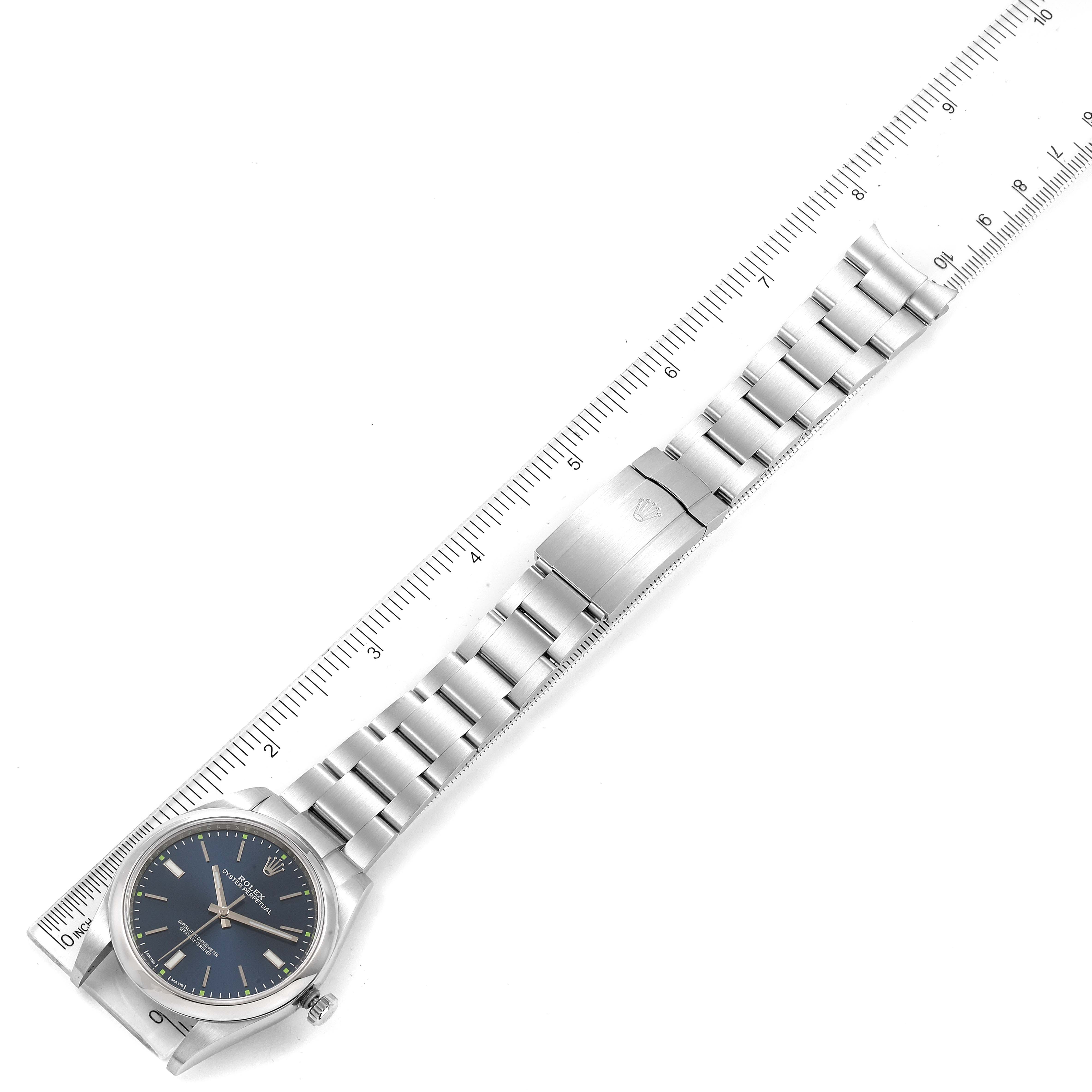 The image shows a full view of a Rolex Oyster Perpetual 114300 Men
s Stainless Steel Blue Dial 114300 Men
s Stainless Steel Blue Dial watch, displaying the face, bracelet, and clasp, aligned with a ruler for scale.