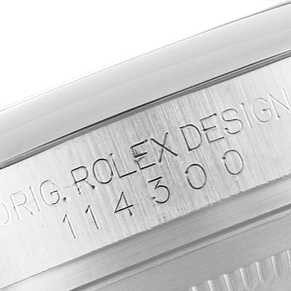 The image shows a close-up of the side case of a Rolex Oyster Perpetual 114300 Men
s Stainless Steel Blue Dial 114300 Men
s Stainless Steel Blue Dial watch, displaying the "ROLEX DESIGN" engraving and model number.
