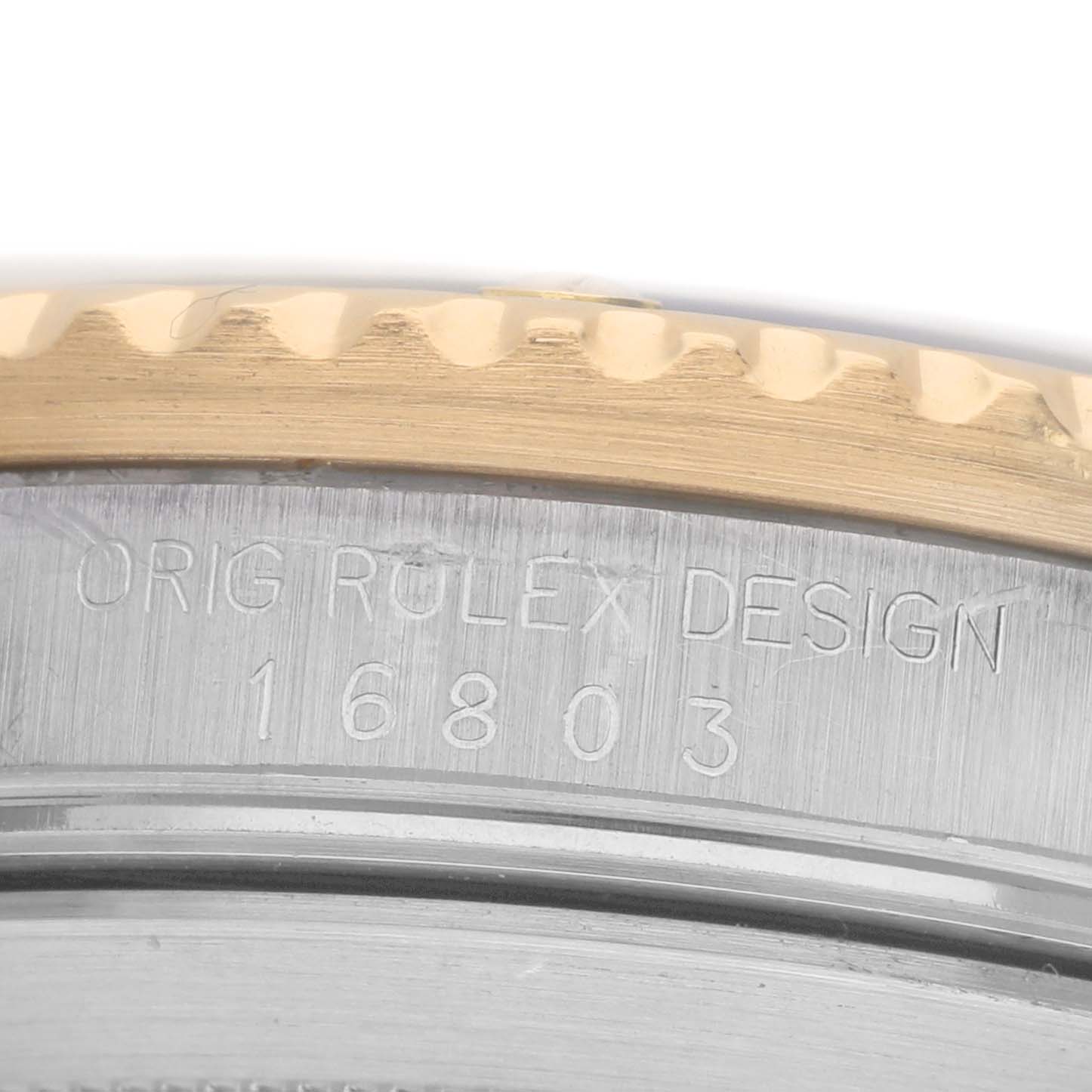 The image shows a close-up of the side of a Rolex Submariner 16803 Men's Steel and Gold (two tone) Black Dial, focusing on the engraved model number 16803 and part of the bezel.