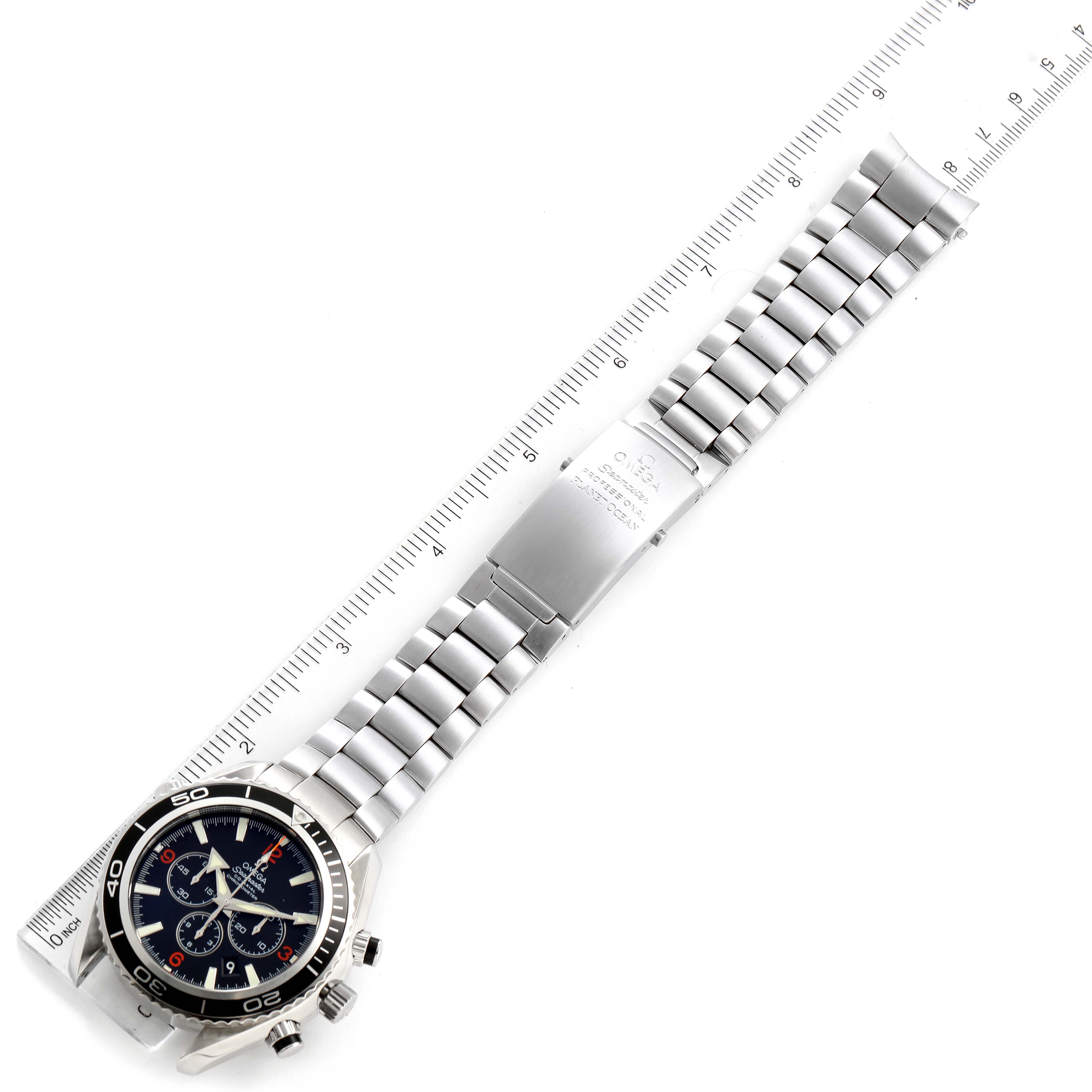 The image shows an Omega Planet Ocean 2210.51.00 Men's Stainless Steel Black Dial 2210.51.00 Men's Stainless Steel Black Dial watch, displaying its face, bezel, and full metal bracelet alongside a ruler for scale.