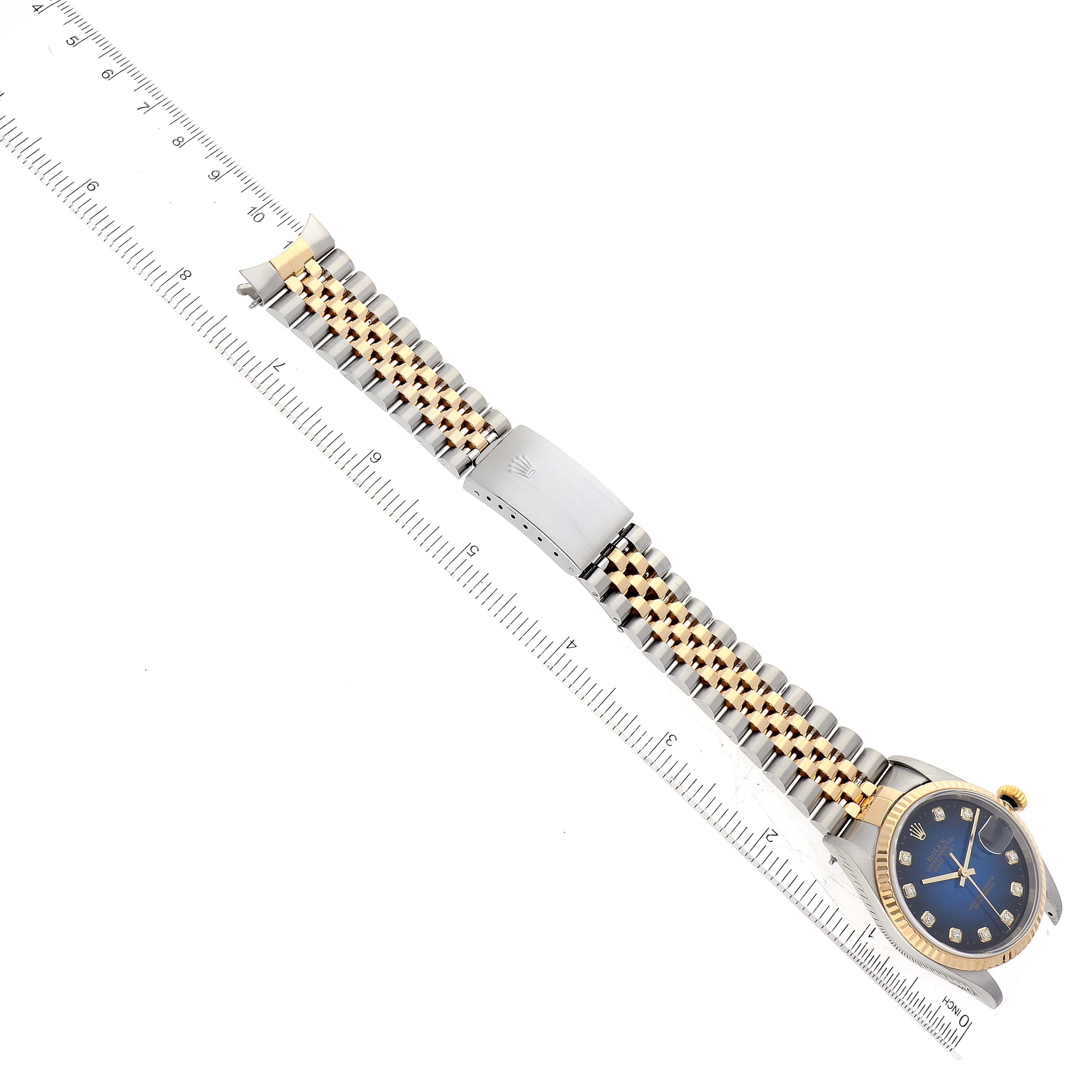 The Rolex Datejust 16233 Men's Steel and Gold (two tone) Blue Dial 16233 Men's Steel and Gold (two tone) Blue Dial watch is shown from a top-down angle, featuring its full band, face, and a metal ruler beside it.