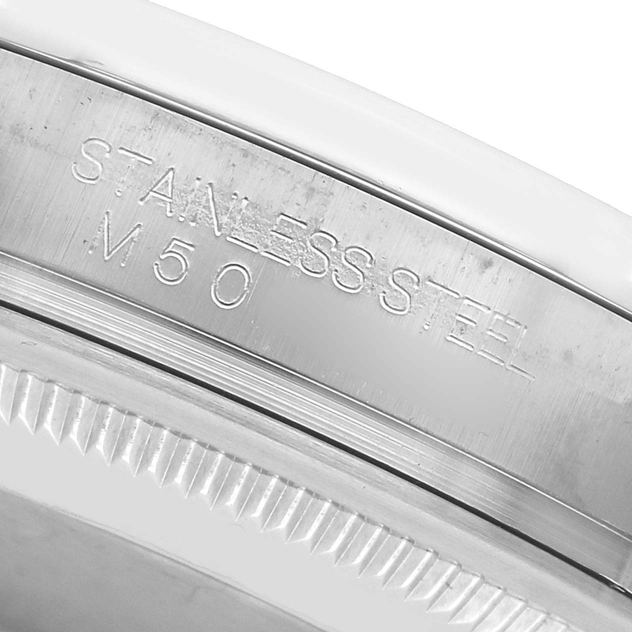 The image shows an angled close-up of the Rolex Datejust 116200 Men
s Stainless Steel White Dial
s stainless steel bezel and edge, highlighting its engravings.