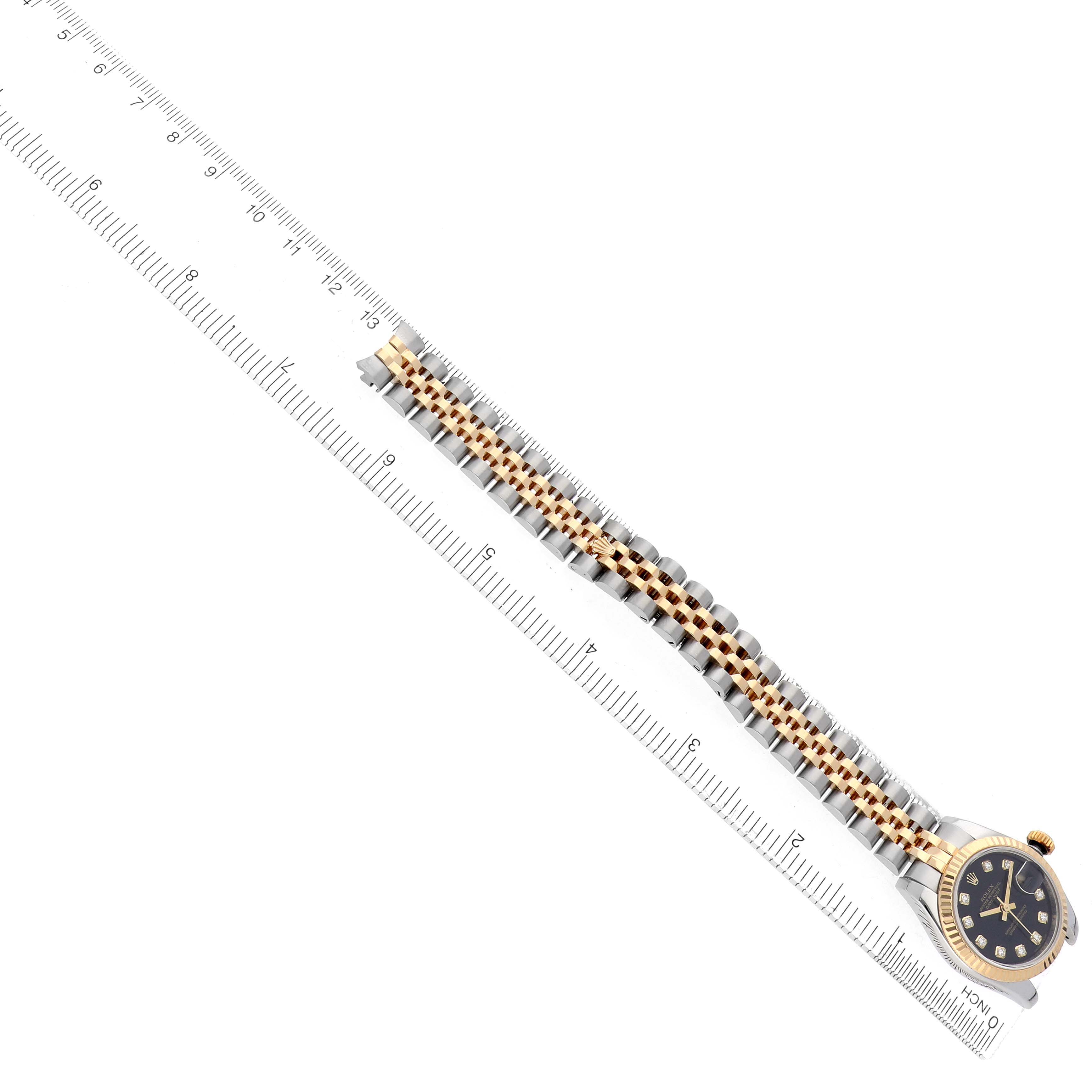The image shows a Rolex Datejust 179173 Women's Steel and Gold (two tone) Black Dial watch laid alongside a ruler, highlighting its two-tone bracelet and dark dial with diamond markers.