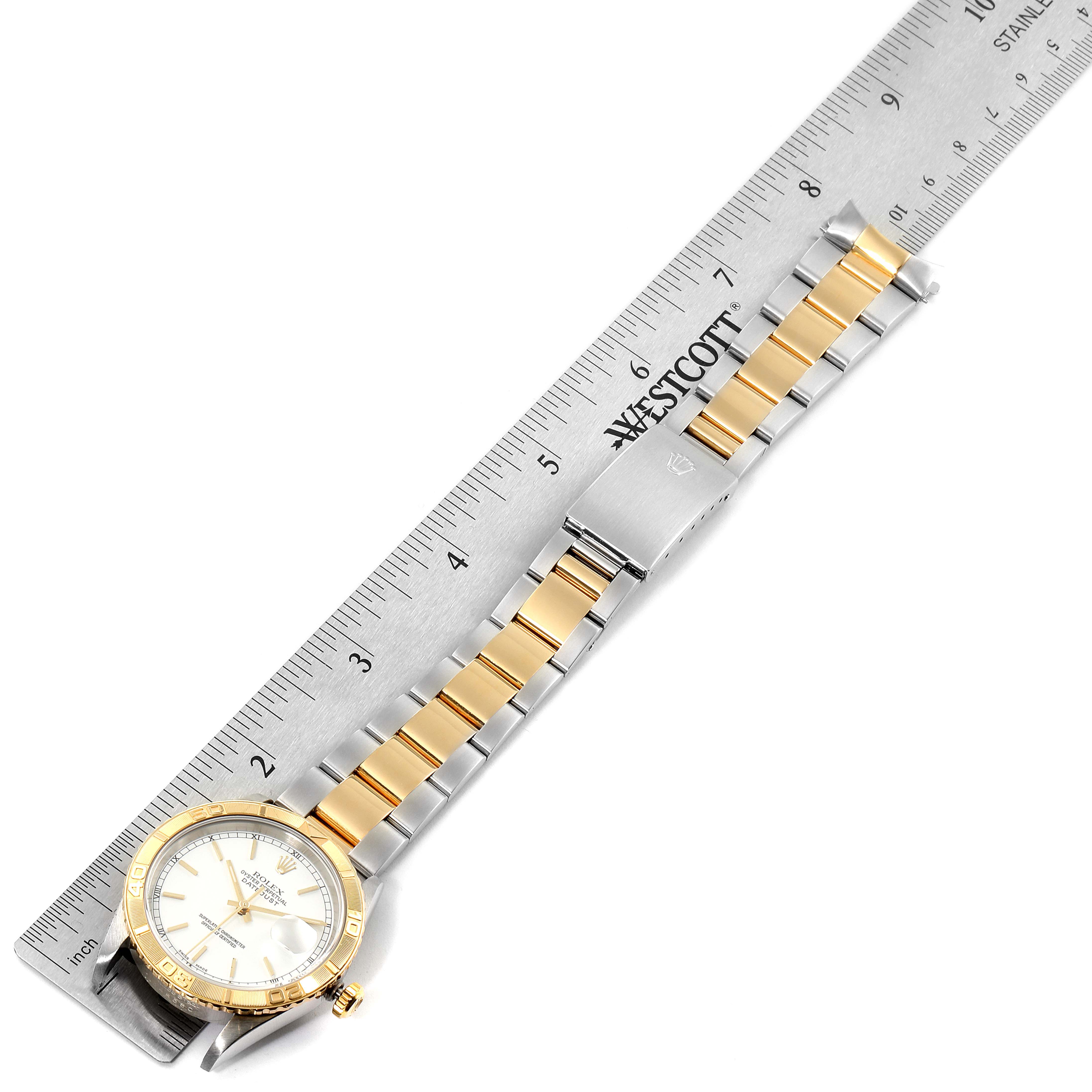 The Rolex Turn-o-Graph 16263 Men
s Steel and Gold (two tone) White Dial 16263 Men
s Steel and Gold (two tone) White Dial watch is shown from a top-down angle, featuring its face, bezel, and bracelet alongside a ruler.