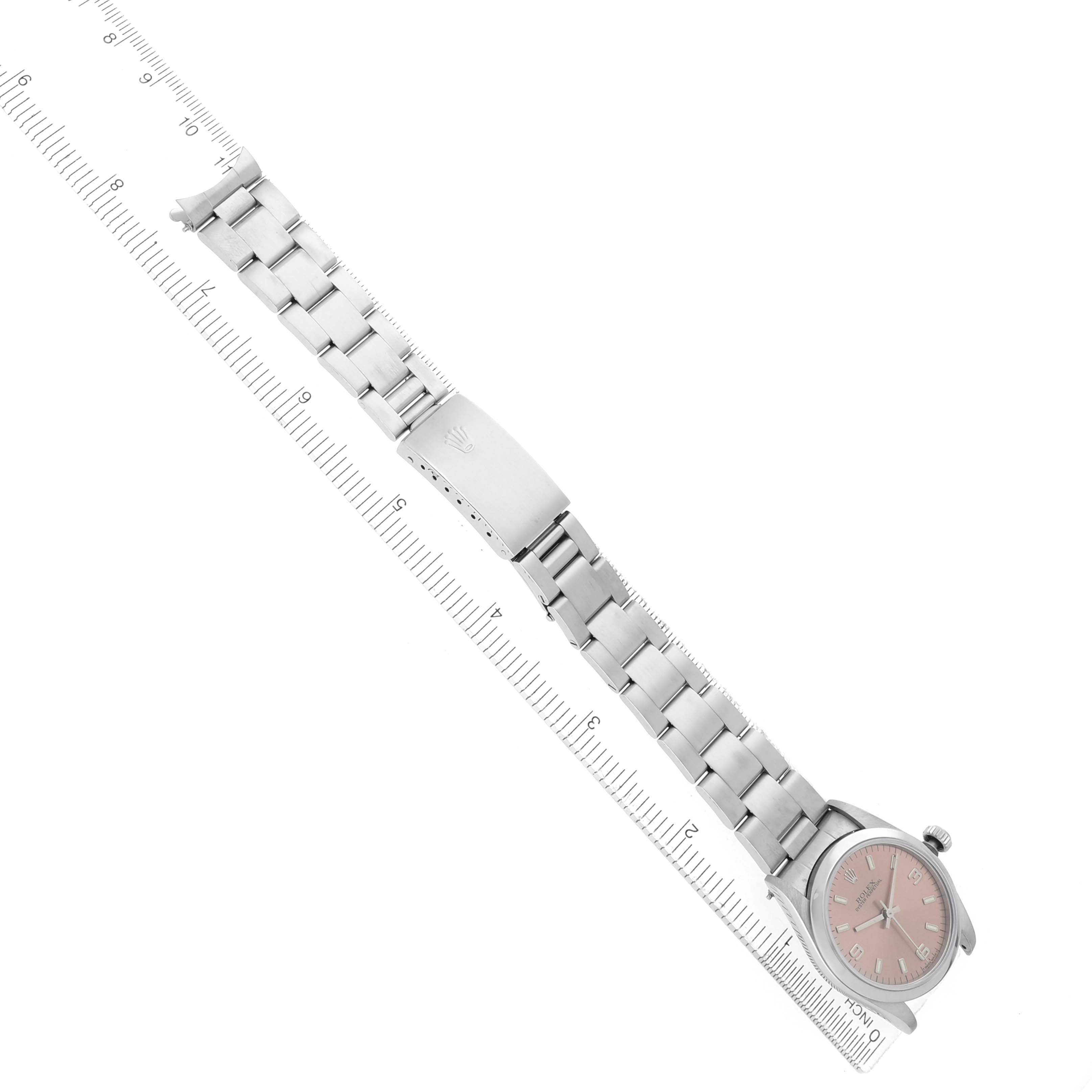 The image shows a Rolex Mid-Size 67480 Women's Stainless Steel Pink Dial watch at an angled top view, highlighting the bracelet, clasp, and face alongside a ruler.