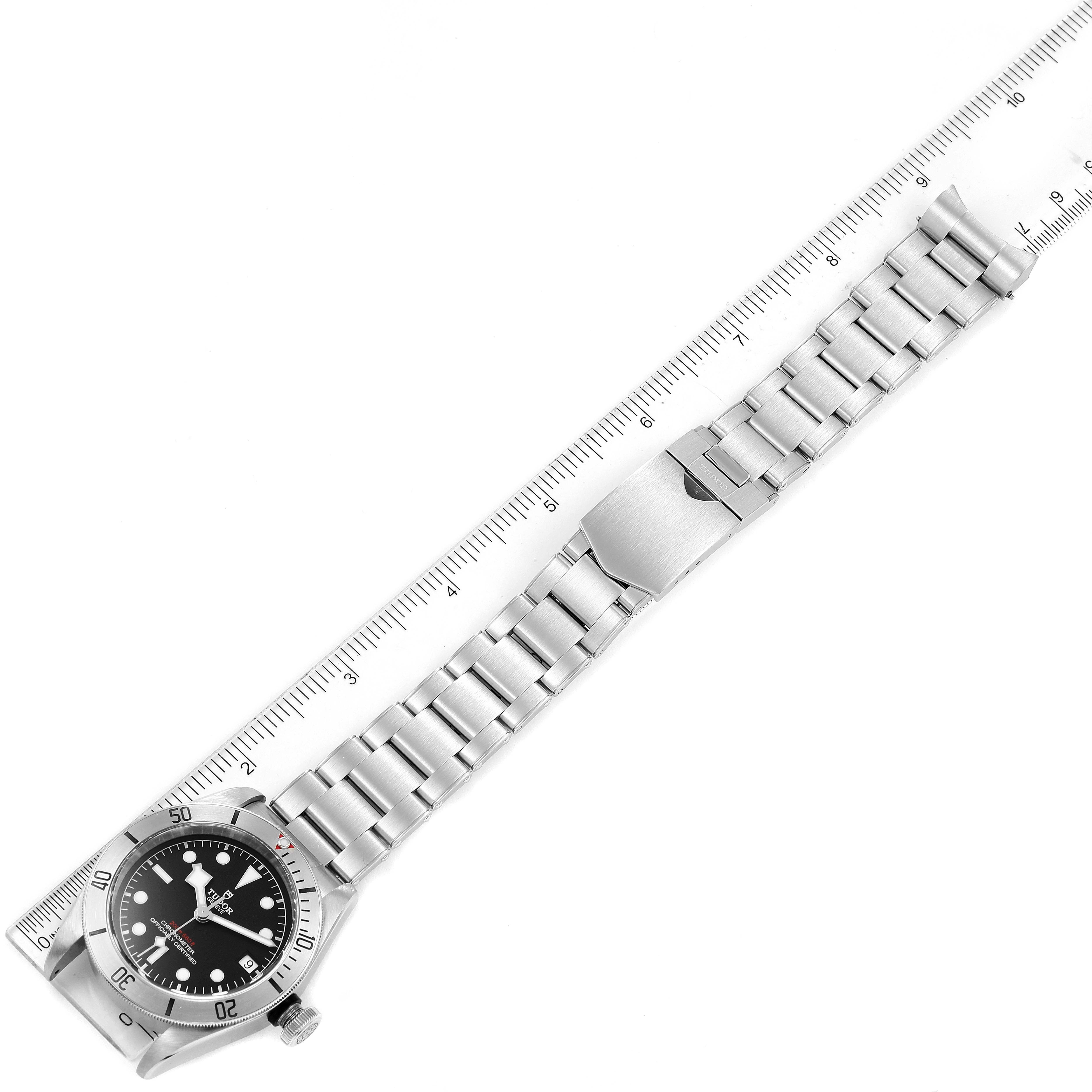 The Tudor Heritage Black Bay 55020 Men's Stainless Steel Black Dial 55020 Men's Stainless Steel Black Dial watch is shown from a top-down angle, including its stainless steel bracelet and clasp parallel to a ruler for scale.