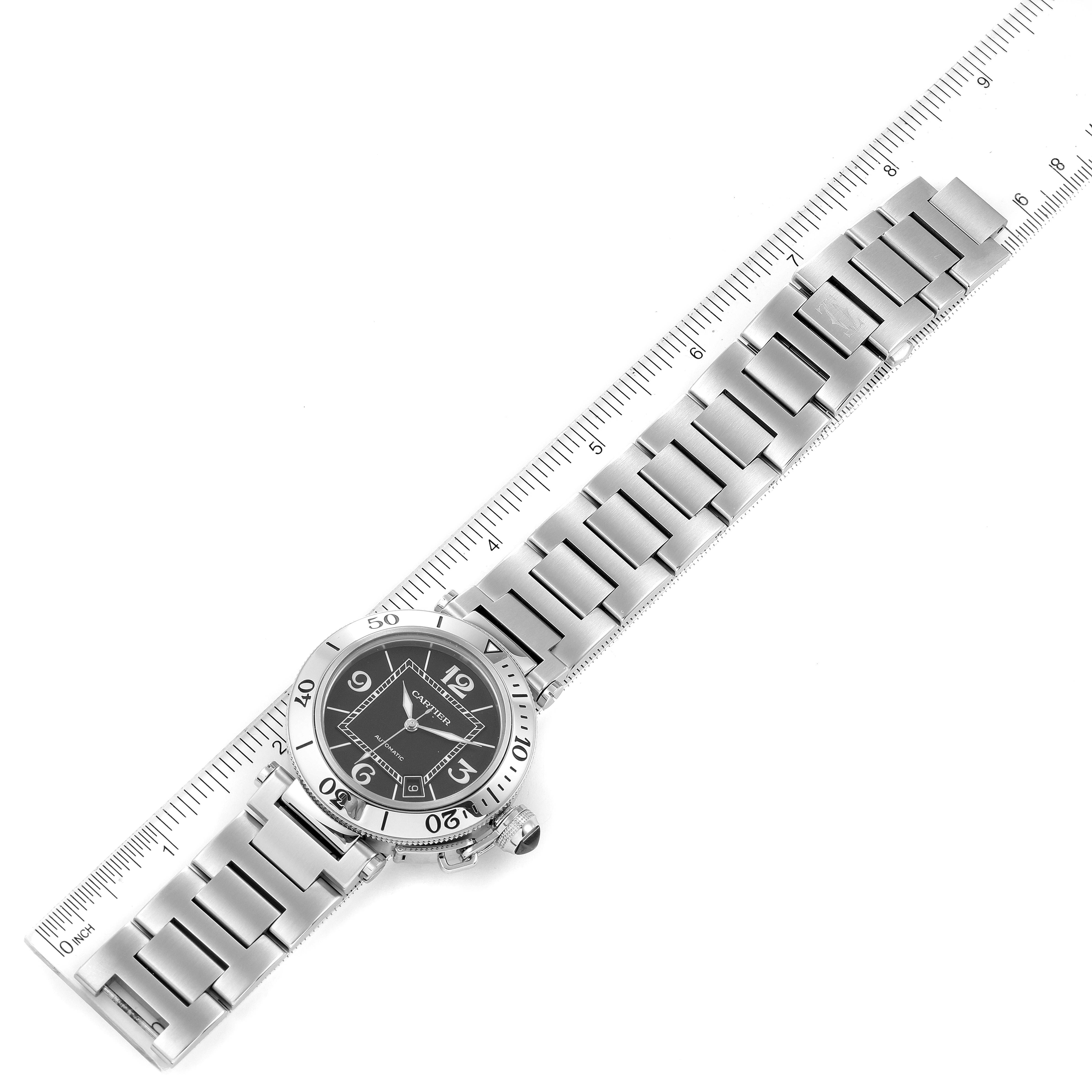 The image shows a full view of a Cartier Pasha W31077M7 Men's Stainless Steel Black Dial W31077M7 Men's Stainless Steel Black Dial watch lying flat with its metal bracelet and face alongside a measuring ruler.